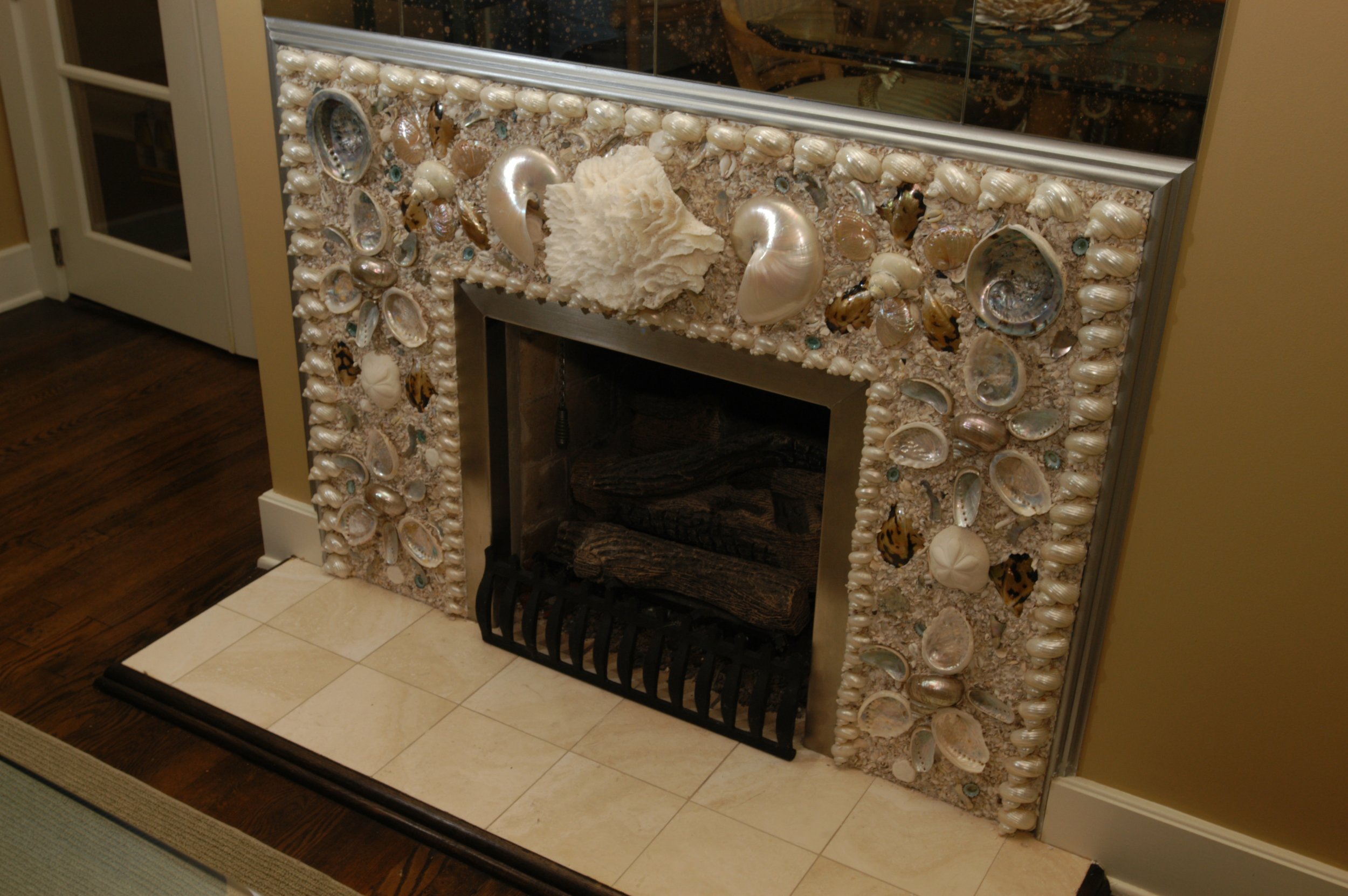 Decorative fireplace surrounded by shells, pearls, and seashells with a mirror above and a wood log inside.