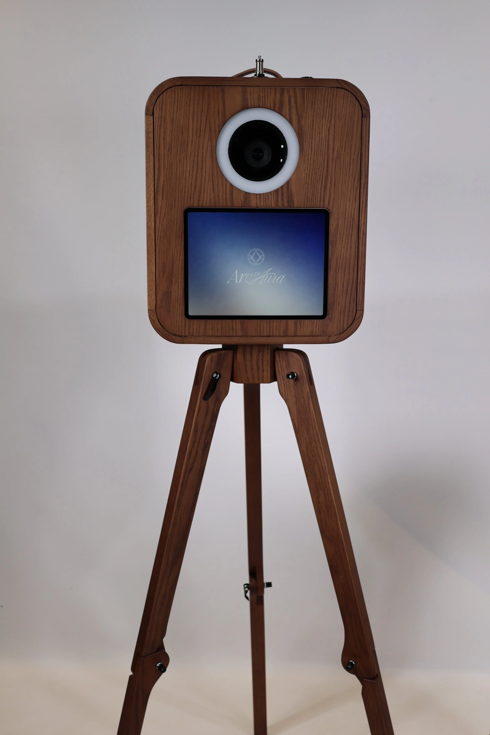 A digital camera for an event photo booth on a tripod stand with a circular and a screen displaying the Arc & Aura Event Media Company logo.