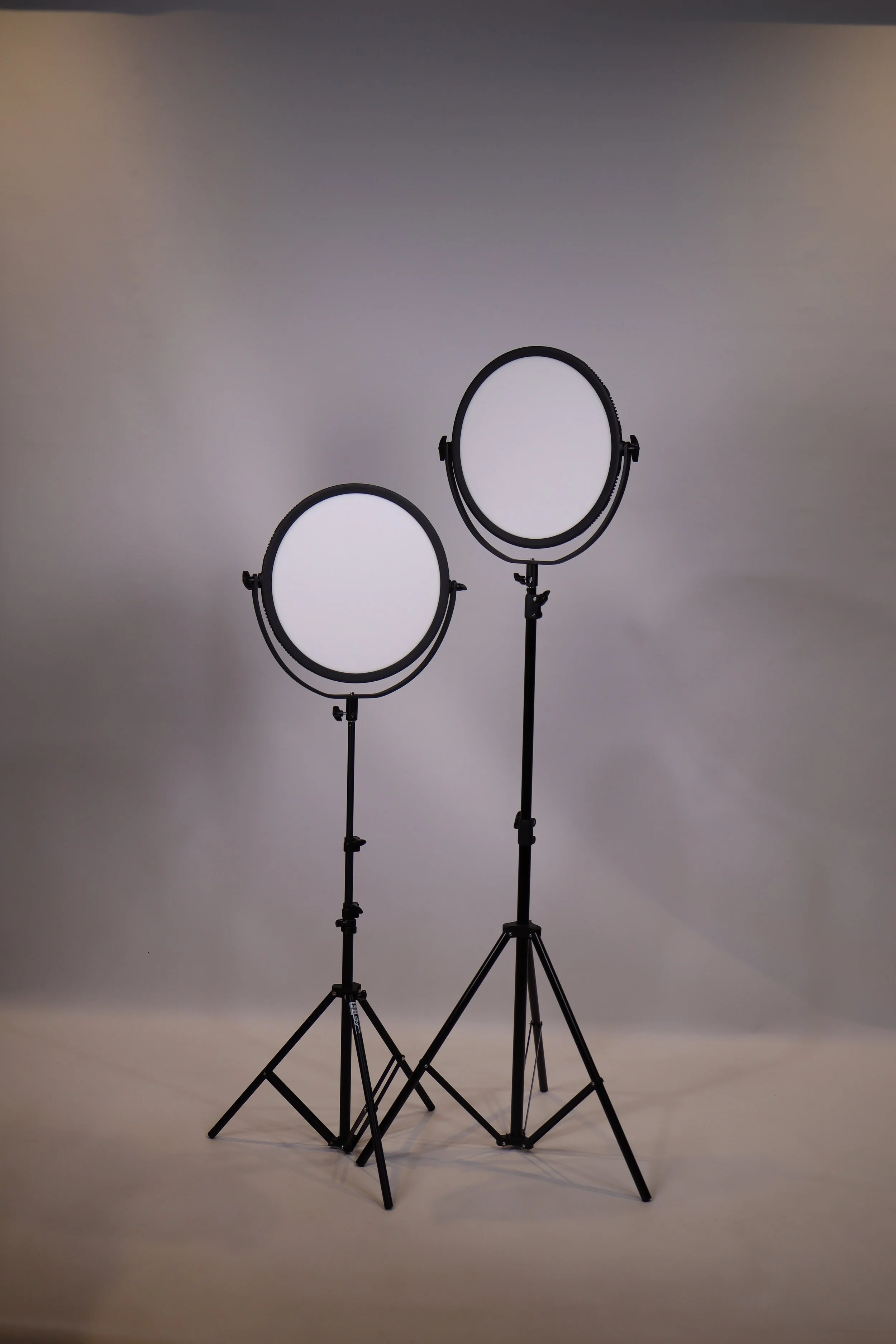 Two studio lights with circular diffusers on stands against a plain background.
