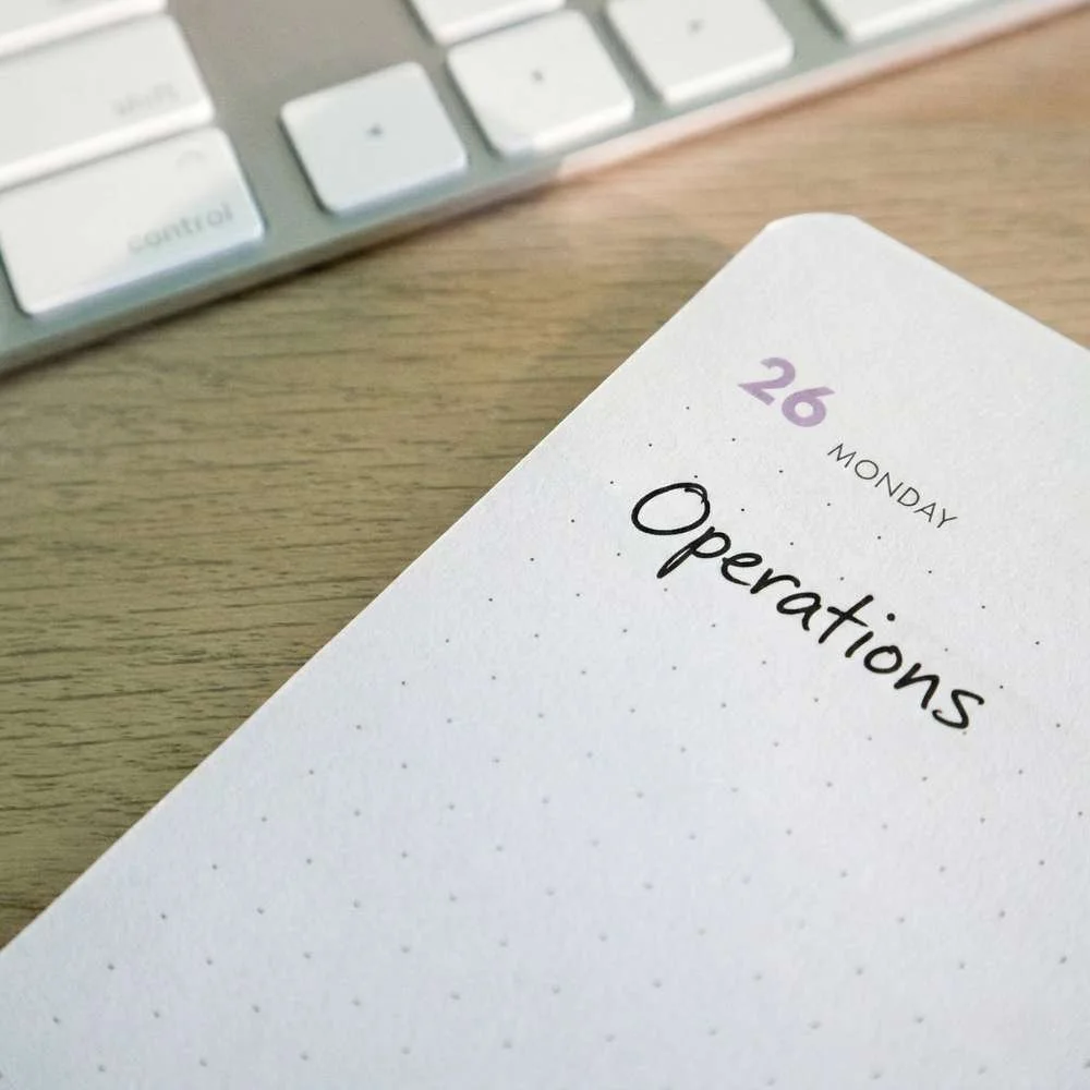 A planner page with the date Monday, the 26th, and the word "Operations" written on it, placed on a desk near a keyboard.