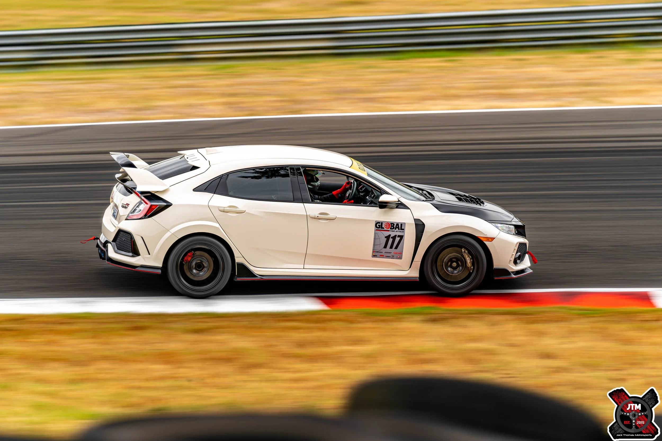 A white racing car with black accents speeding on a race track, with a driver wearing a helmet inside, and a racing number 107 on the side.