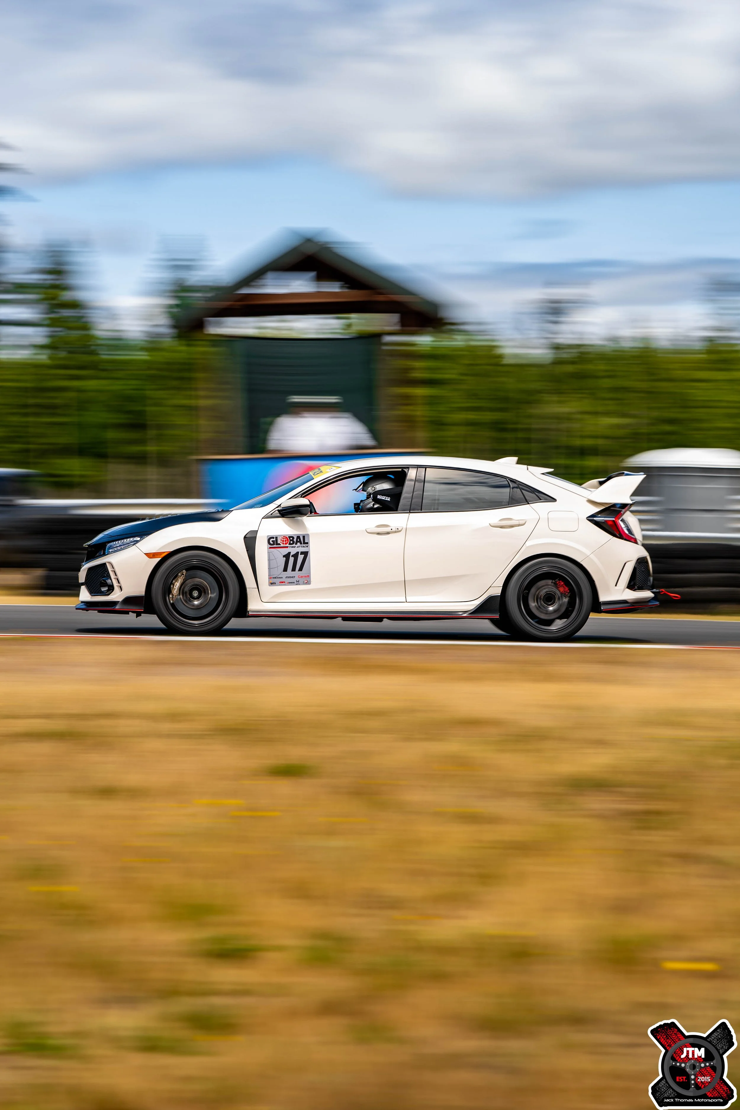 A white race car with the number 117 on its side, speeding on a track with motion blur in the background.
