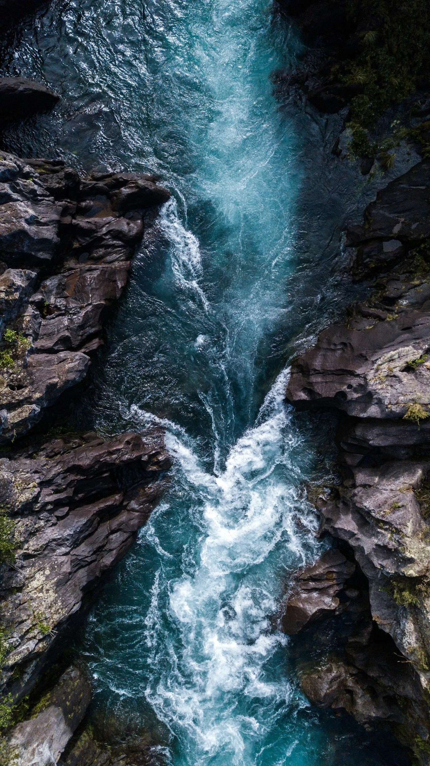 Aerial view of a narrow mountain river rushing through rocky canyon with foam and turbulence.