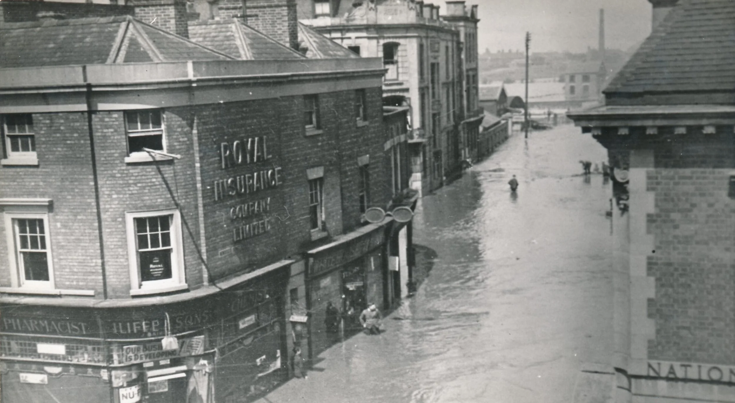 Photo taken from Barclays Bank of the May 1932 floods. The view is down Newdegate Square where the statue of George Eliot now stands.  You can see the Newdegate Arms Hotel just behind Iliffes Chemist and behind that the Cattle Market.