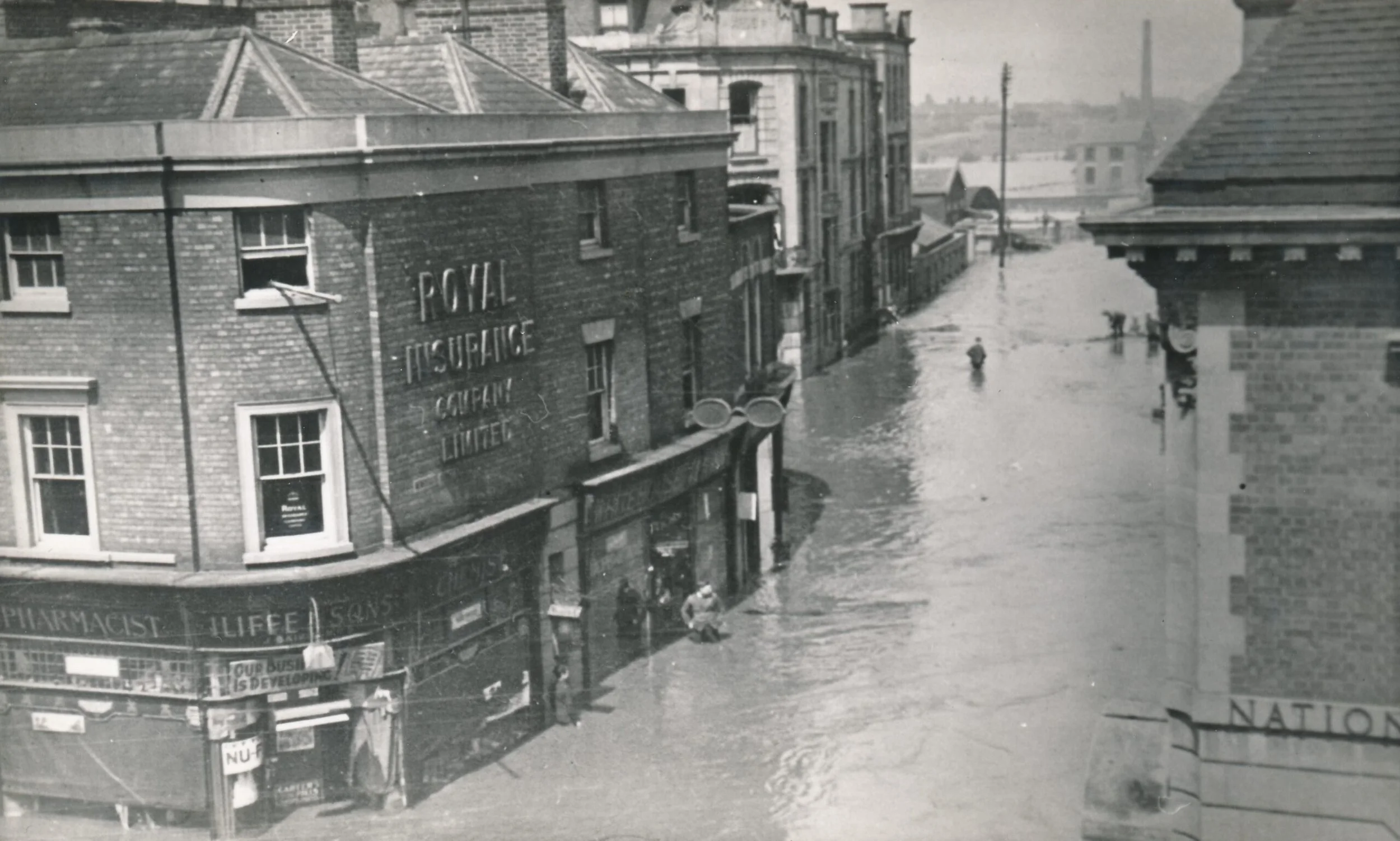 Newdegate Street Nuneaton in the floods of May 1932. Iliffes Pharmacy is on the left with the Royal Insurance Society above it.  At the back of Iliffes is the Newdegate Arms Hotel (demolished in the late 60's) and behind that the cattle market and ra