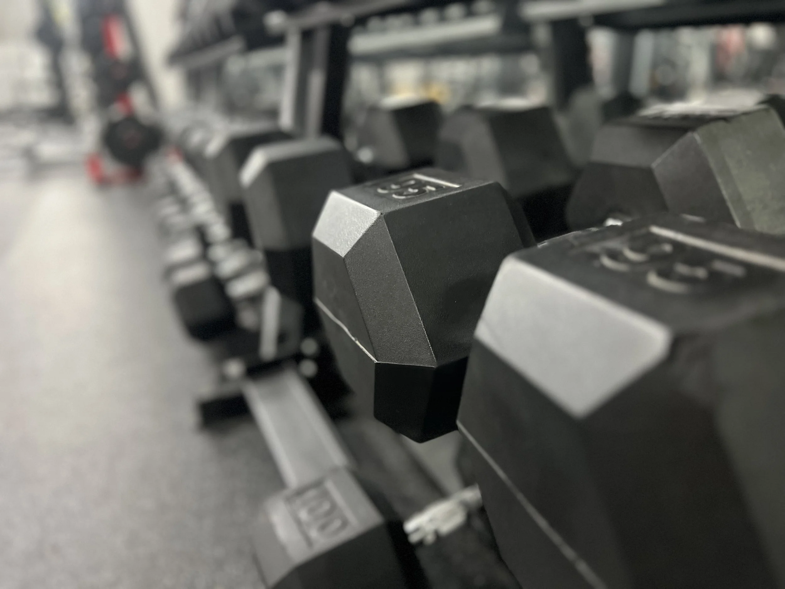 Black hexagonal dumbbells on a rack in a gym.