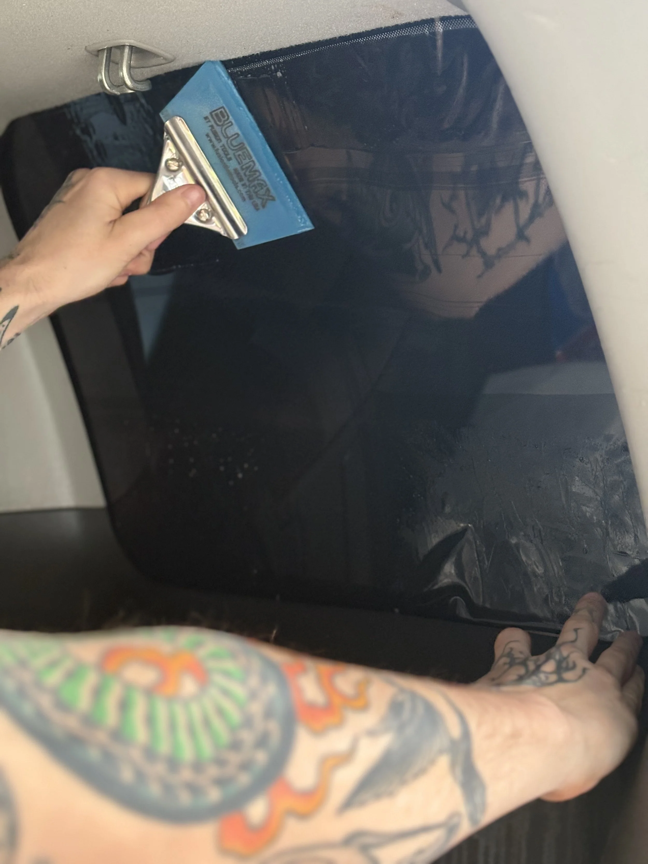 A tattooed arm is pressing a squeegee against a tinted window.