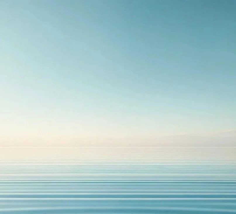 Calm ocean with gentle ripples, clear blue sky, and soft sunlight on the horizon.