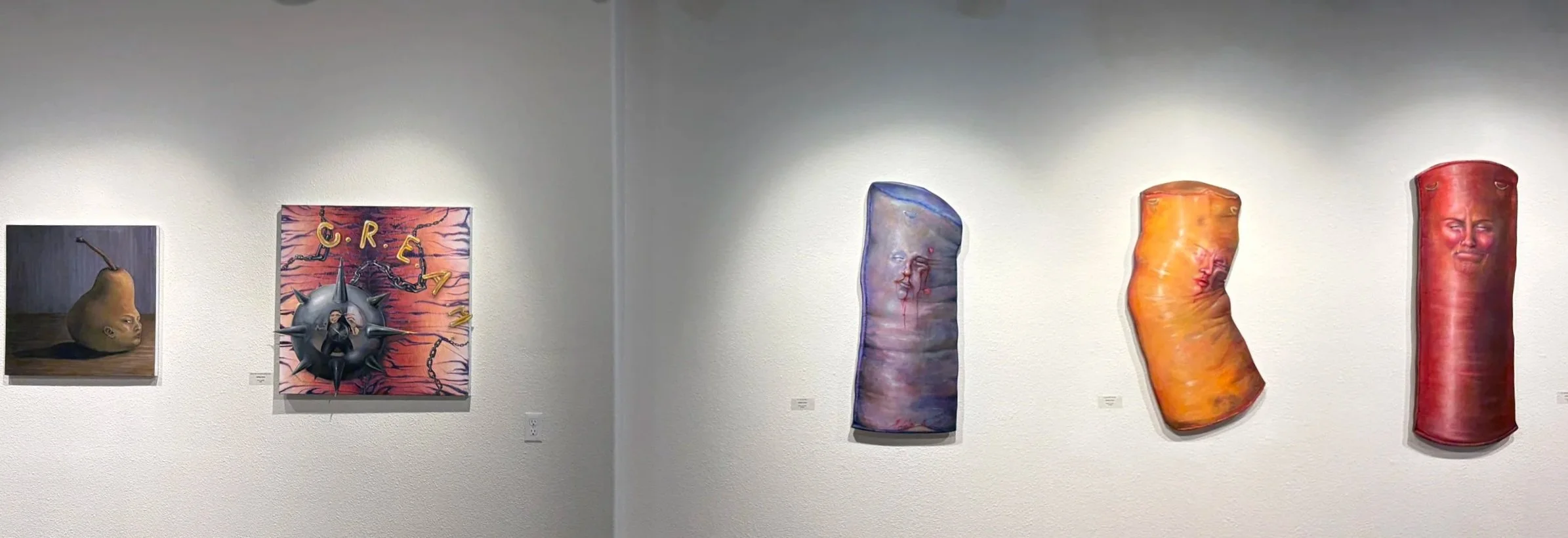 Art exhibition displaying surreal paintings of human-like pears, a spiked ball with a person, and abstract faces, on white walls.