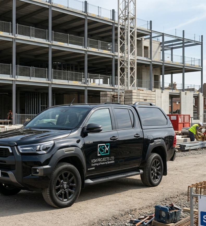 Black pickup truck parked at a construction site, with a partially built multi-story building and construction workers in the background.