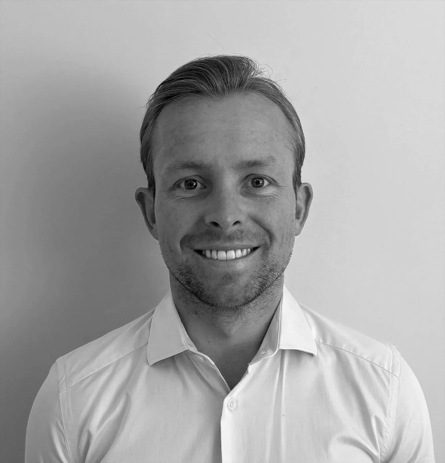Black and white photo of a smiling man with short hair, wearing a collared shirt against a plain background.