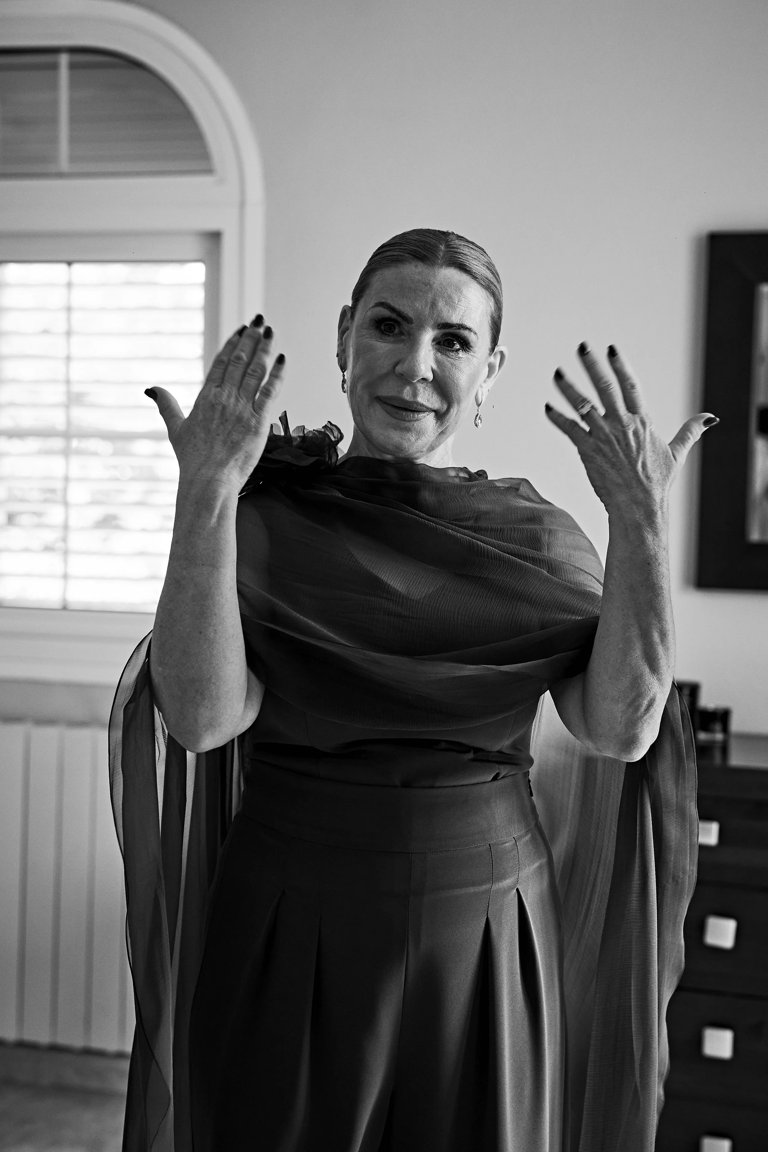 Mujer arreglada con vestido elegante y pendientes, posando dentro de una habitación, en blanco y negro.
