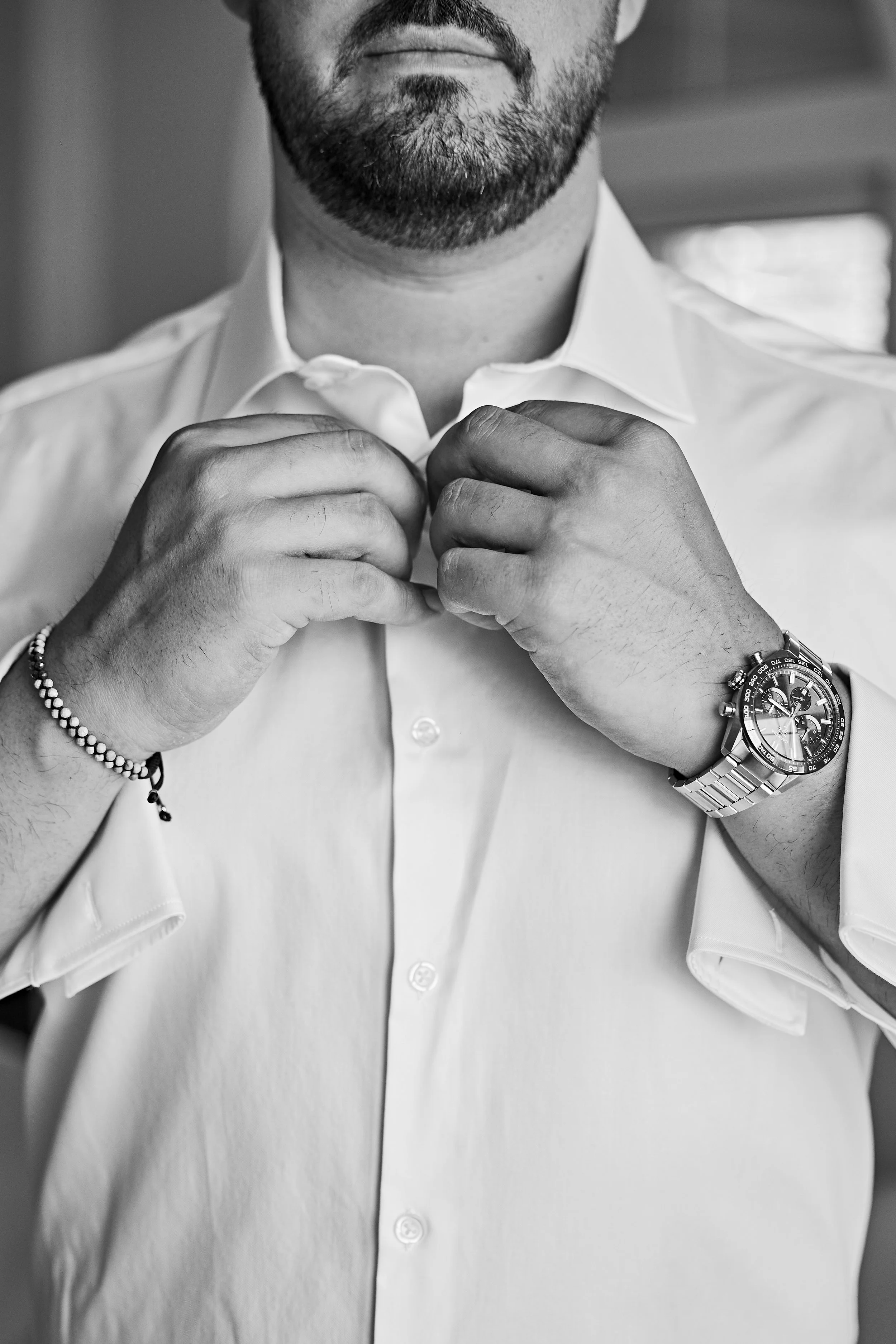 Hombre ajustándose la camisa. Usa reloj en la muñeca derecha y una pulsera en la izquierda.