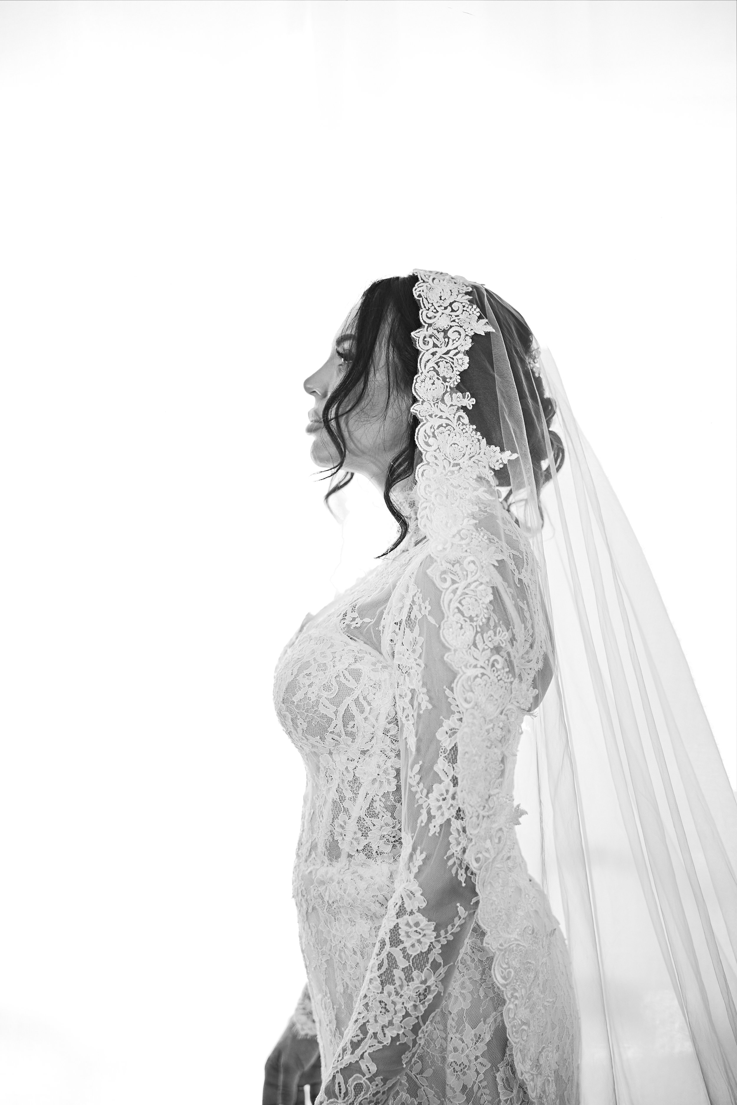 Mujer con vestido de encaje y velo de novia en perfil, negro y blanco.