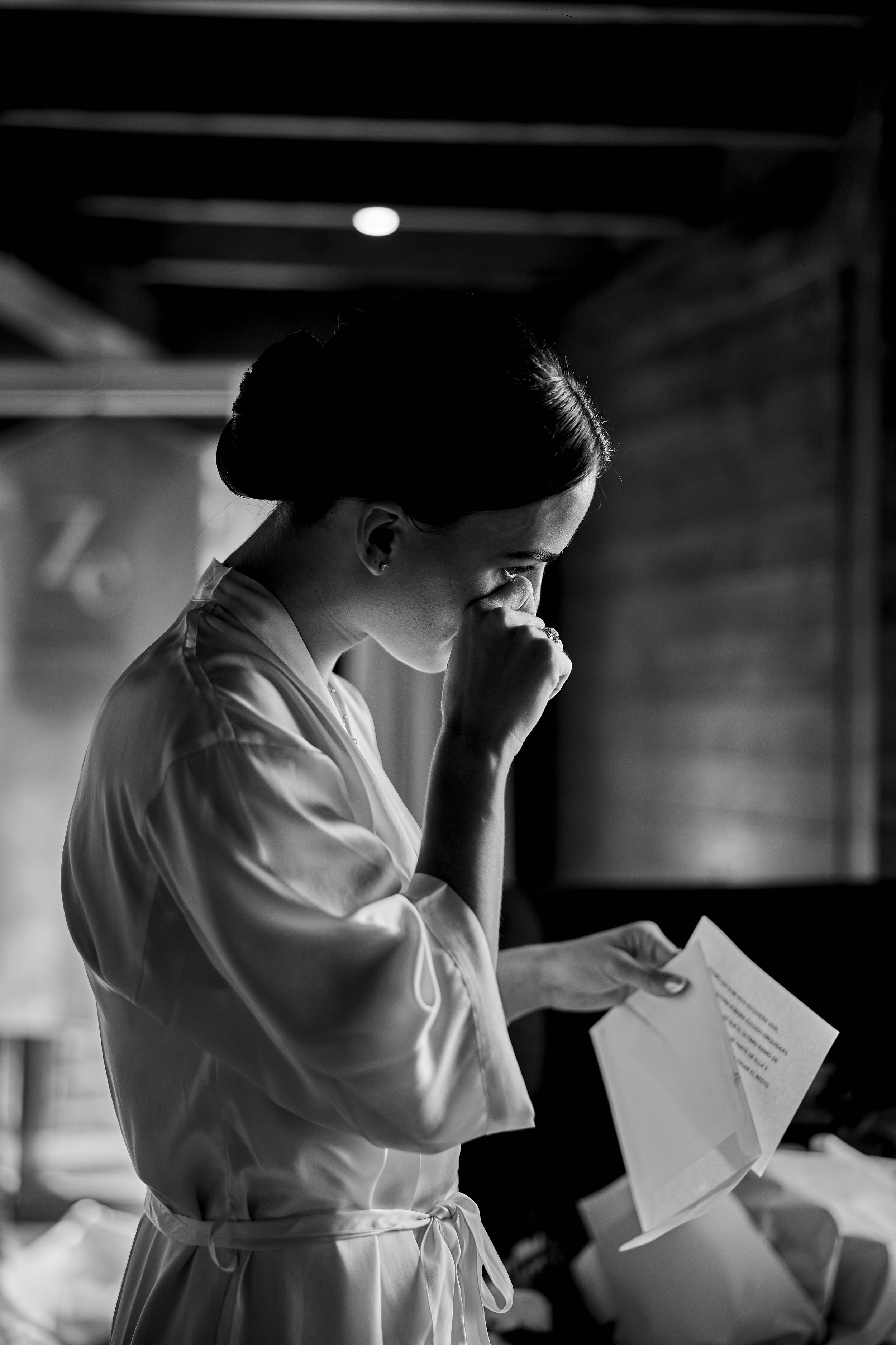 Mujer con peinado recogido y vestido de seda, llorando y sosteniendo una carta en un ambiente oscuro.
