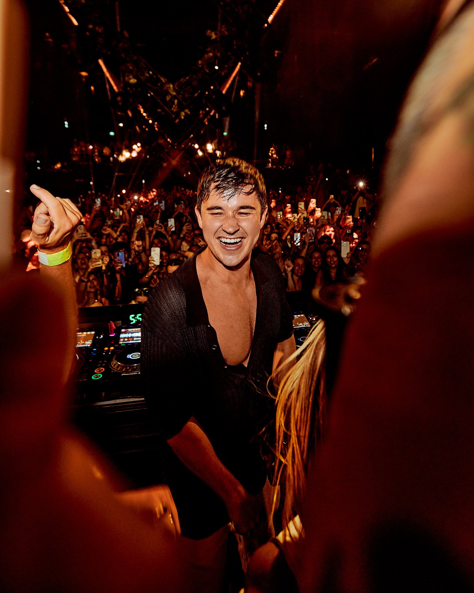 Un DJ sonriente en un concierto con una multitud de personas tomando fotos y disfrutando la música en la noche.