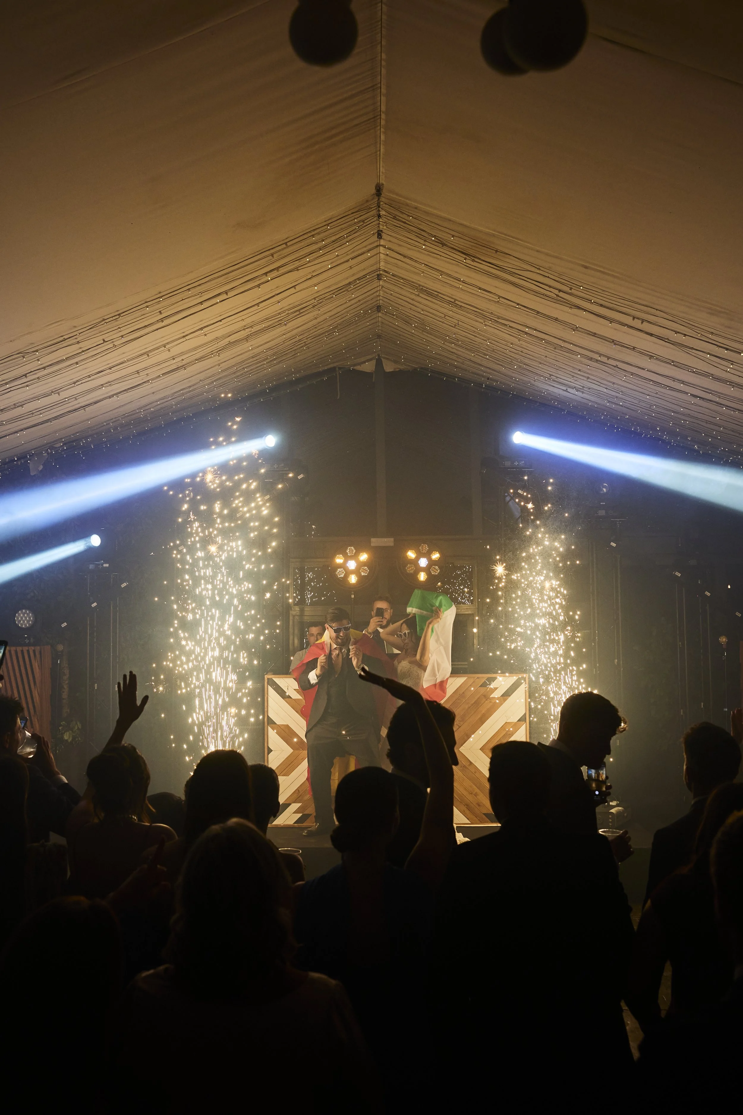 una fiesta con personas bailando y una alfombra de fuegos artificiales en el escenario, con luces y una decoración de techo con cadenas de luces y globos