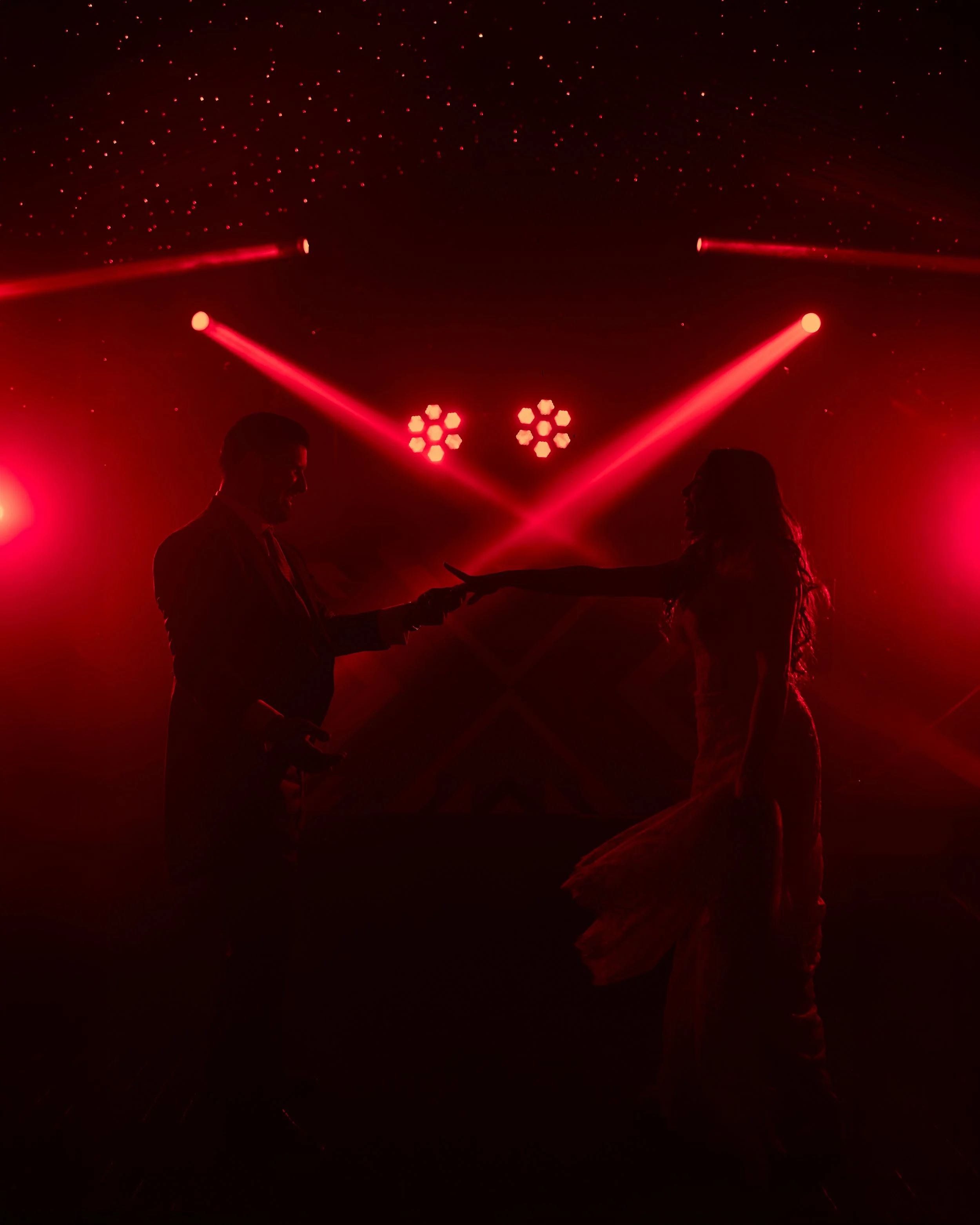 Pareja bailando en un escenario con iluminación roja y efectos de láser, formando un ambiente romántico y festivo.