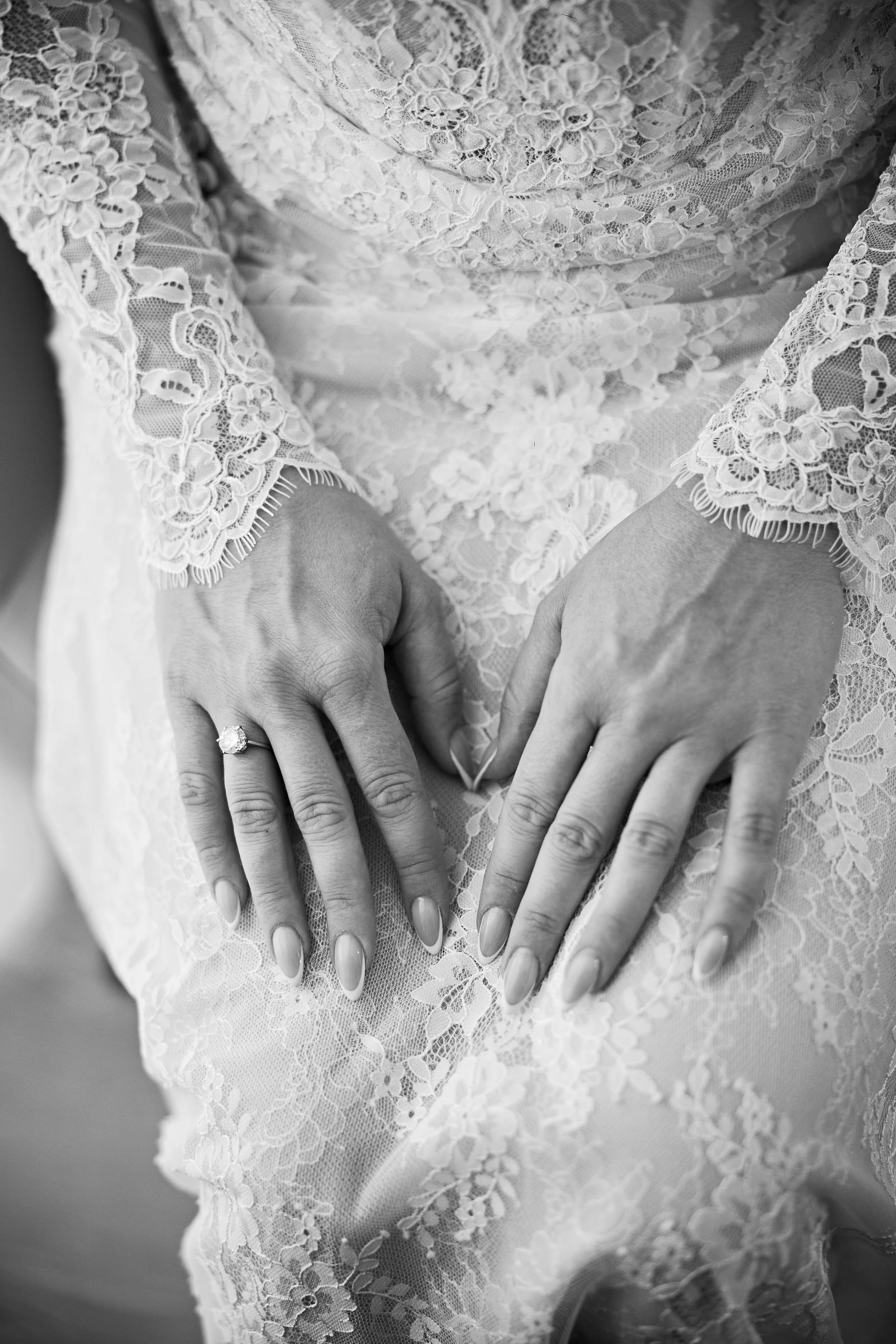Manos de una mujer con vestido de encaje y anillo en el dedo anular, en un encuadre en blanco y negro.