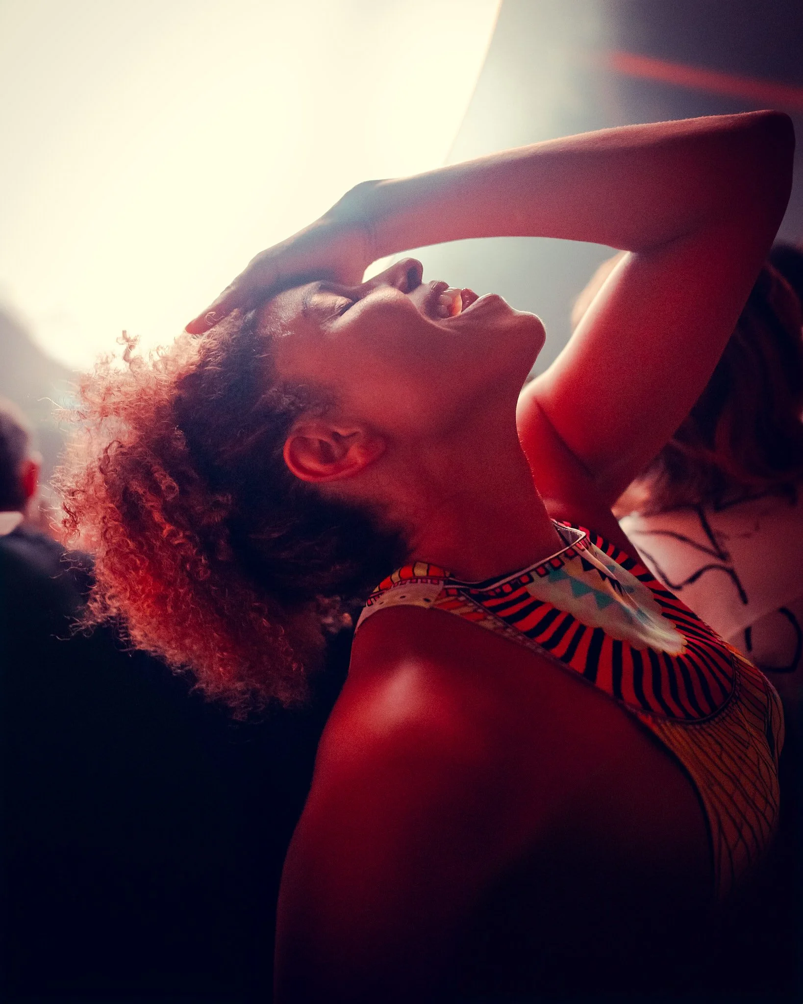Mujer con cabello rizado, sonriendo y con una mano en la frente.