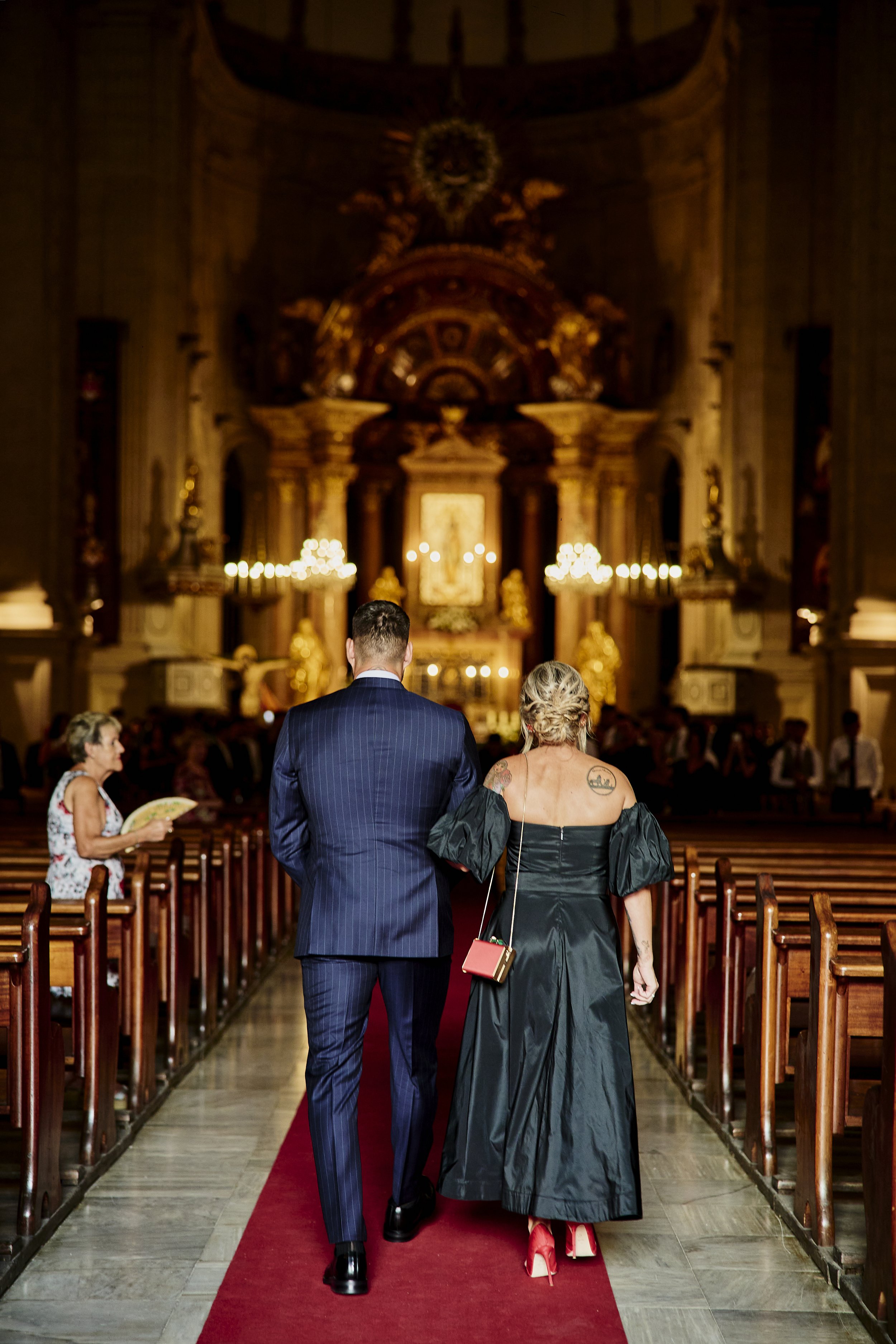 Pareja caminando por el pasillo central de una iglesia decorada para una ceremonia, vista desde atrás.
