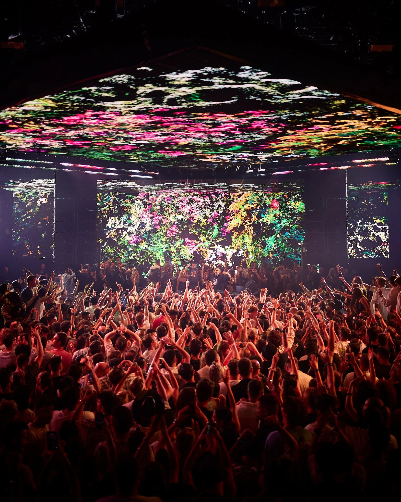 Gran multitud en un concierto con pantallas de iluminación coloridas y una gran pantalla en el escenario.