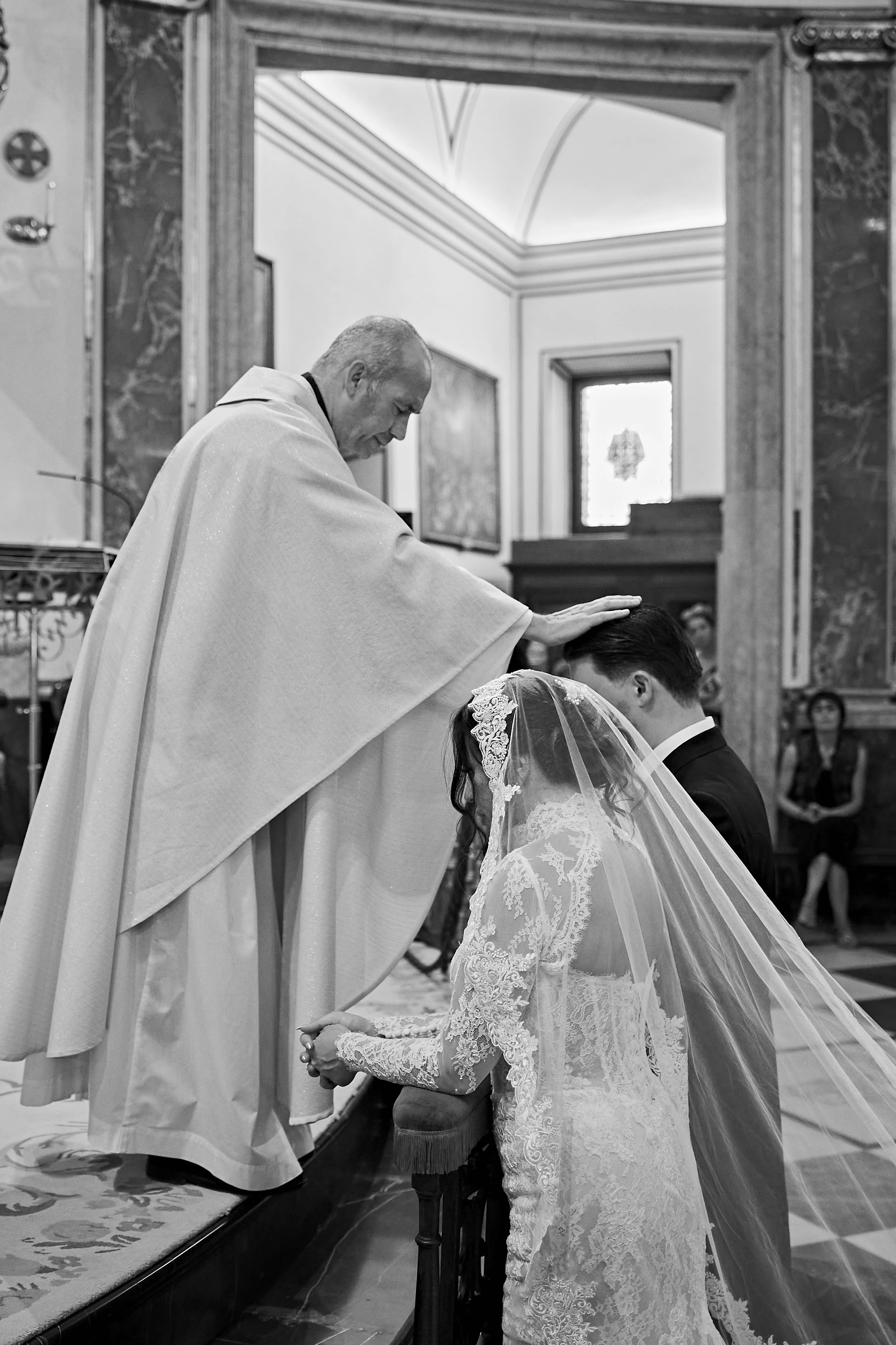 Un sacerdote bendice a una novia con un anillo durante su ceremonia de boda en una iglesia, en un ambiente formal y solemne.