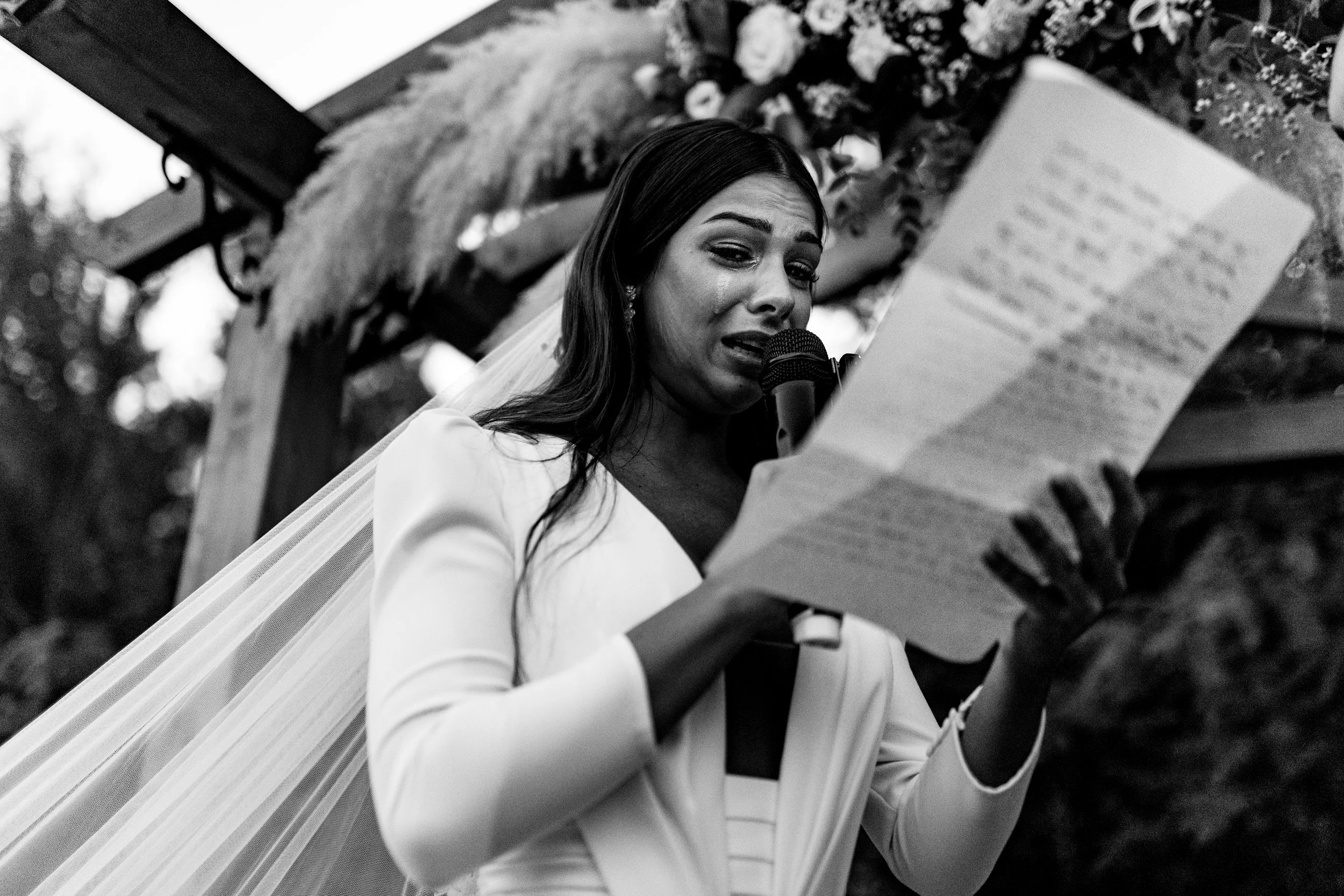 Mujer vestida de novia leyendo un discurso en una ceremonia al aire libre.
