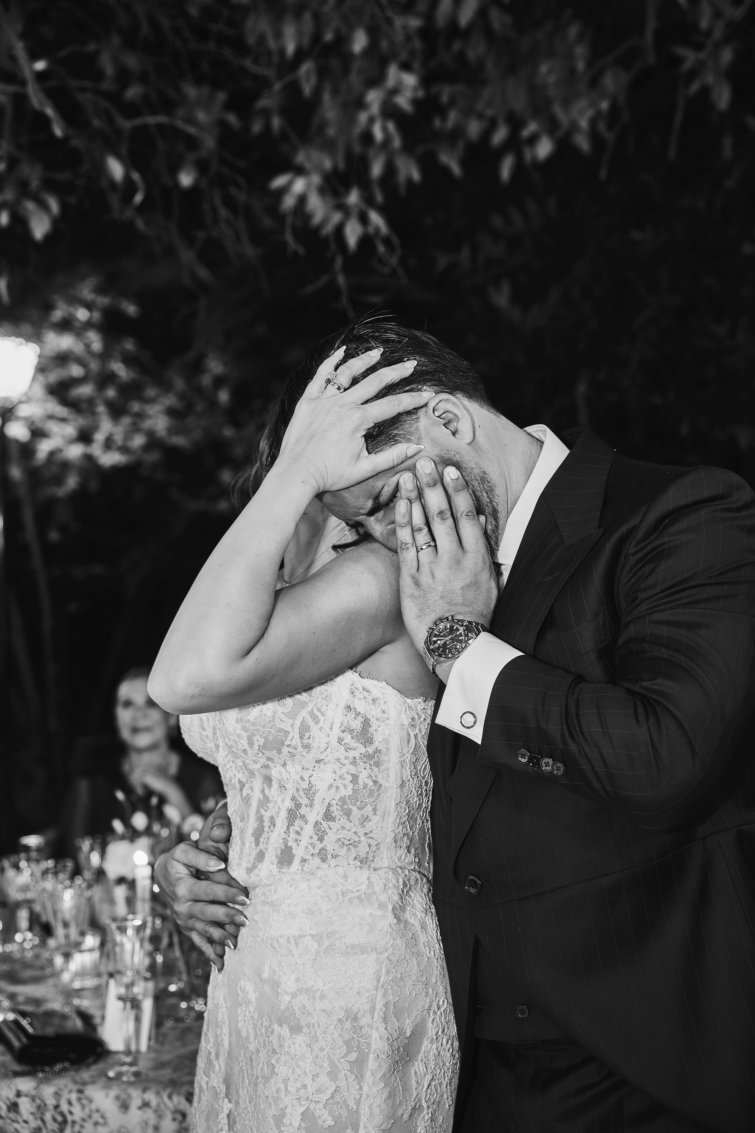 Una pareja en boda bailando y besándose, con fondo de árboles y mesas decoradas.