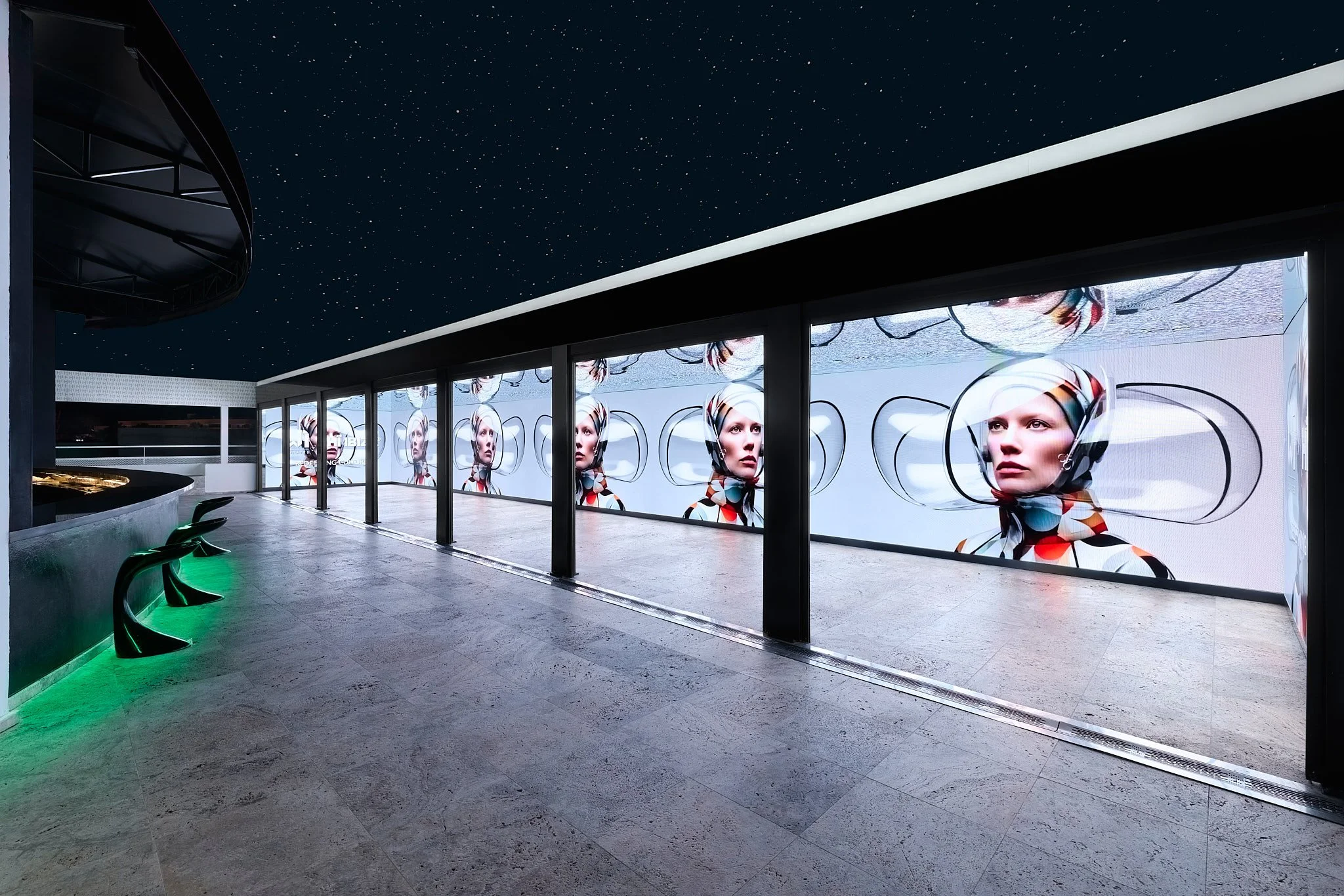 Pantalla digital con rostro de mujer en un espacio moderno con cielo estrellado y suelo de piedra.