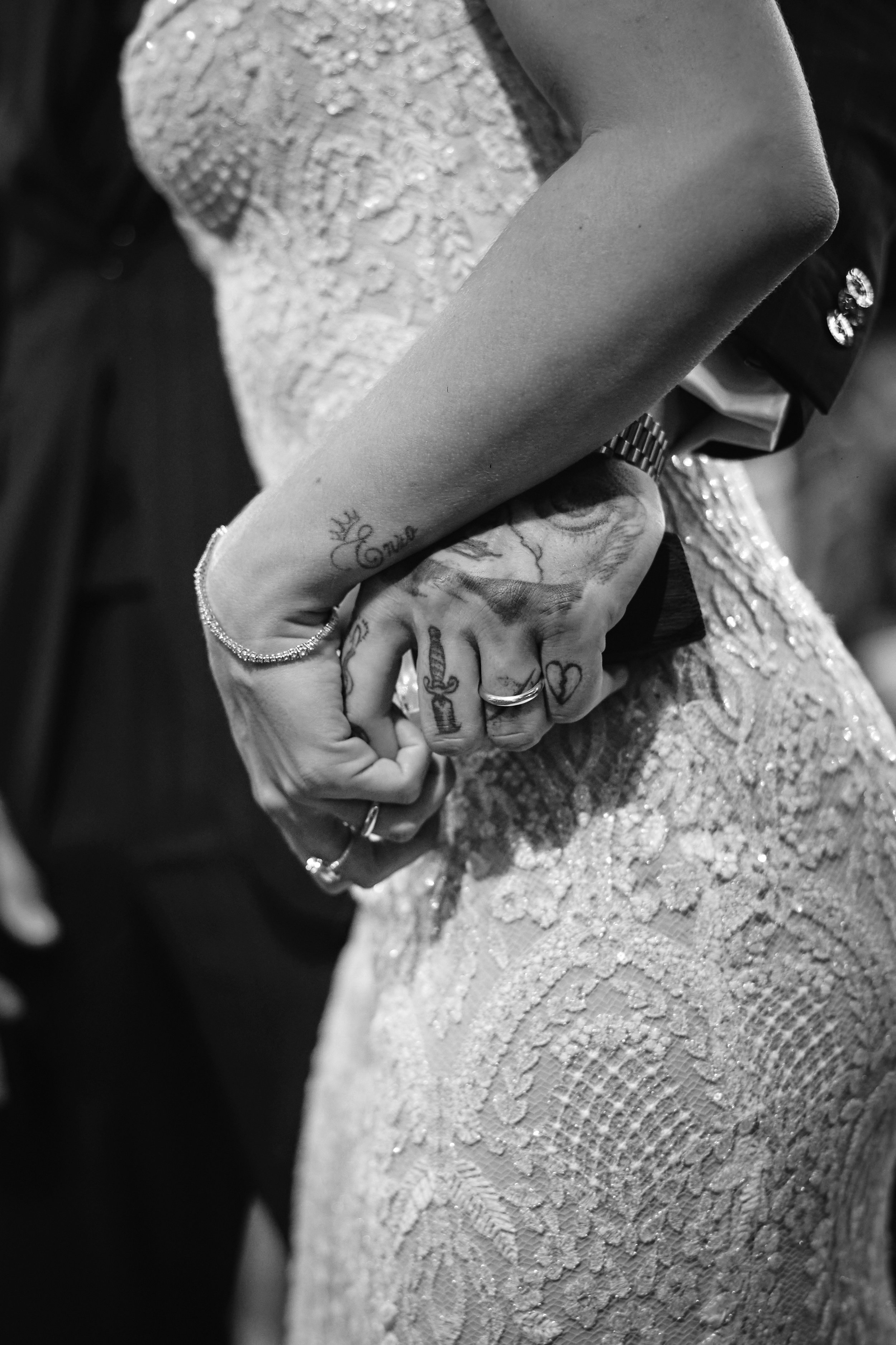 Mano de pareja con tatuajes entrelazadas, con vestido de encaje, en color negro y blanco.