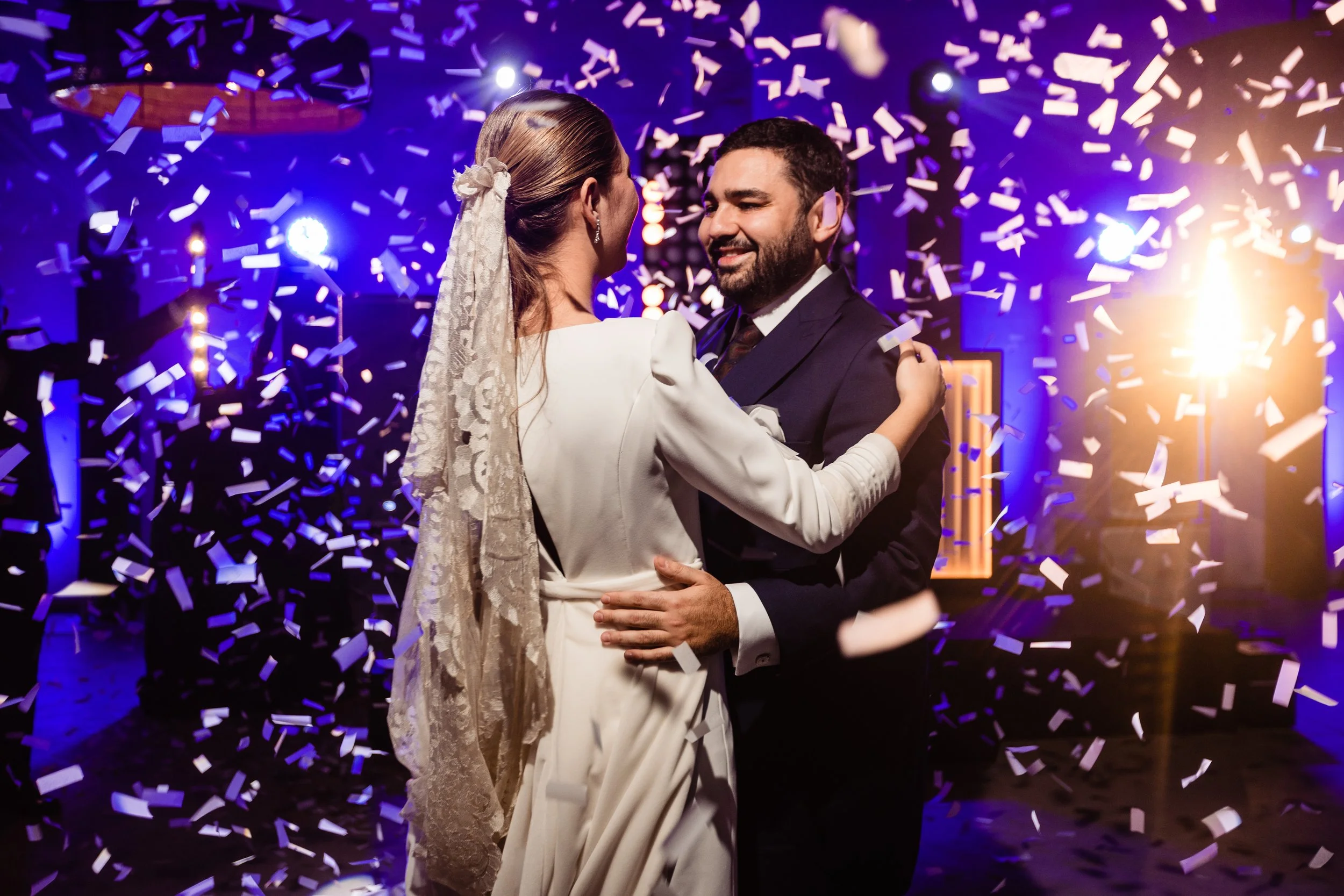 Pareja bailando en boda bajo confeti con luces brillantes.