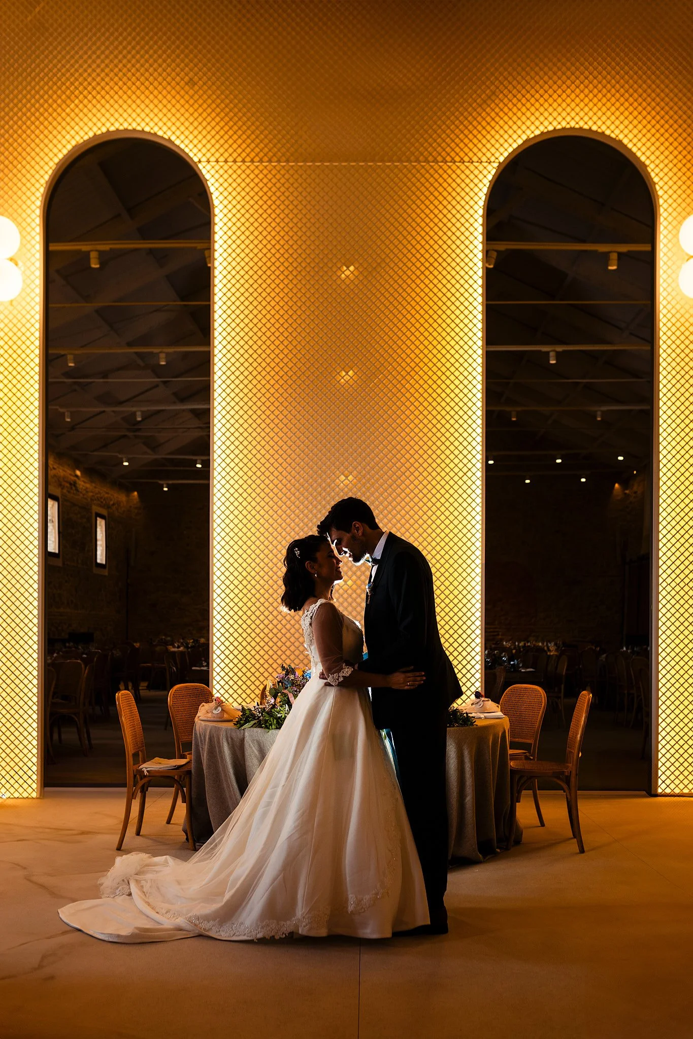 Silueta de joven pareja de novios abrazándose frente a los icónicos arcos luminosos durante un banquete de boda en El Canónigo de Miguel Martí, junto al espacio El Telar, Valencia, mostrando un ambiente elegante y romántico.