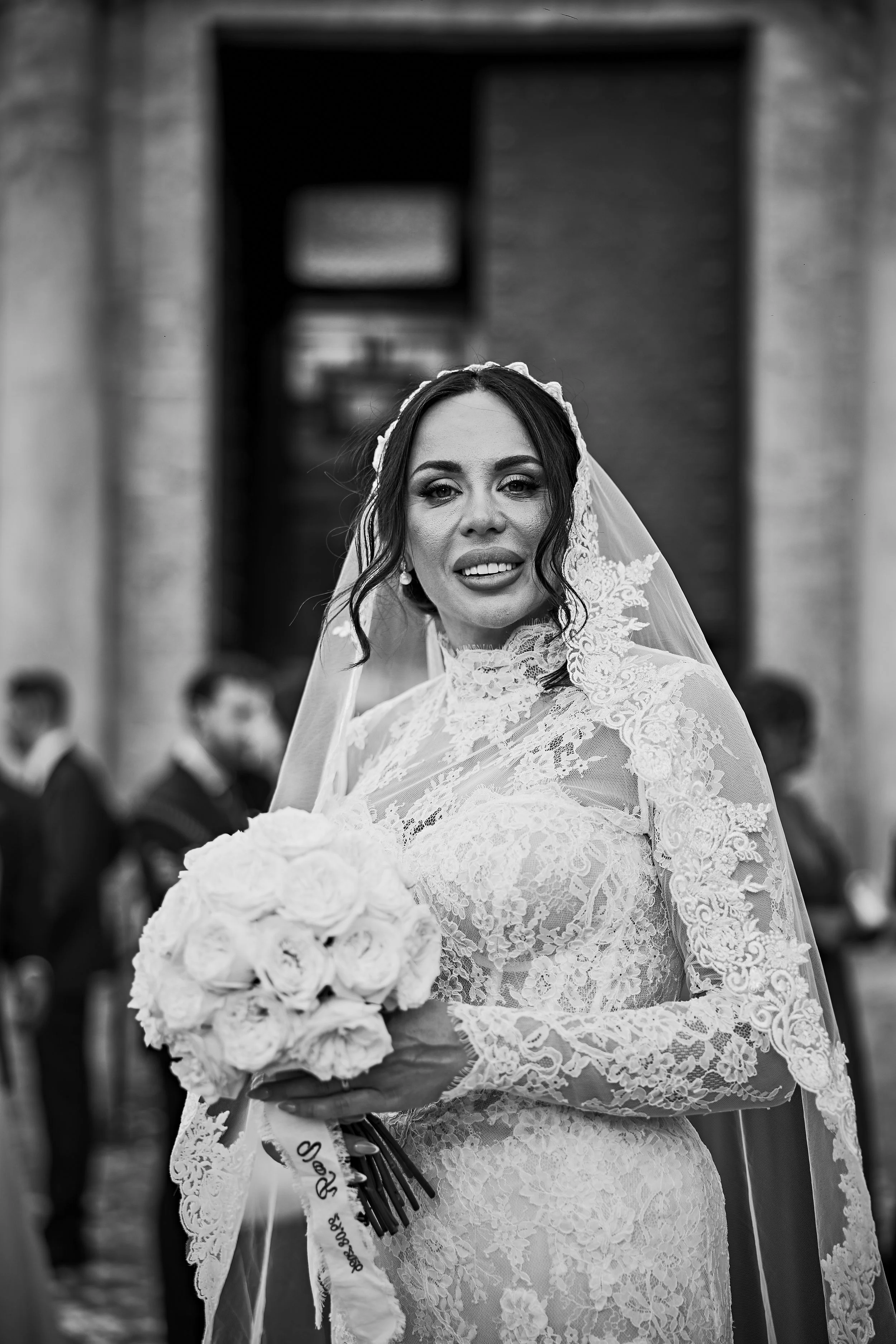 Mujer en vestido de boda con ramo de flores blancas en una ceremonia al aire libre, rodeada de invitados.