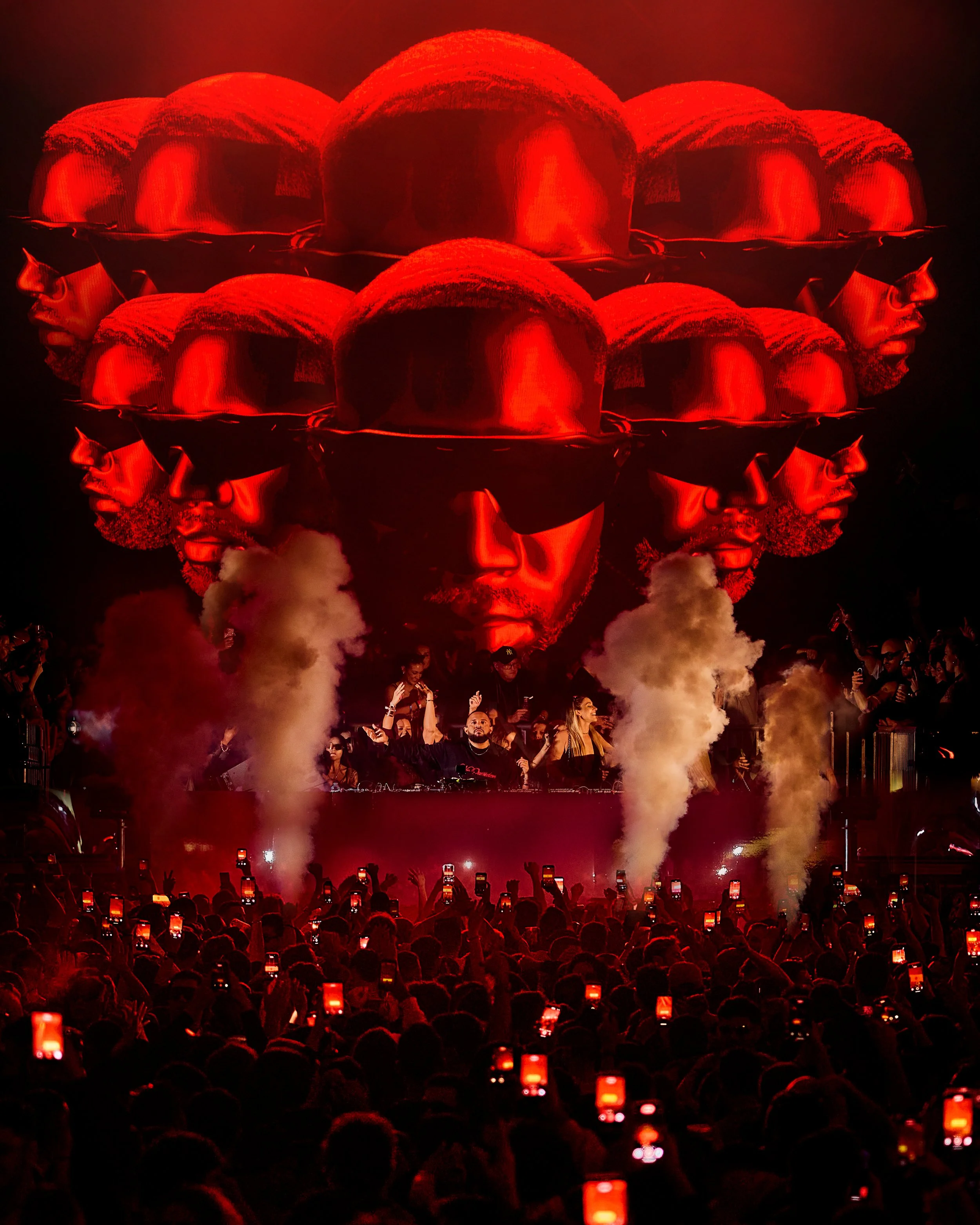 Gordo Escenario con artistas y DJ en un festival de música con pantalla gigante mostrando caras con gafas oscuras y humo rojo.