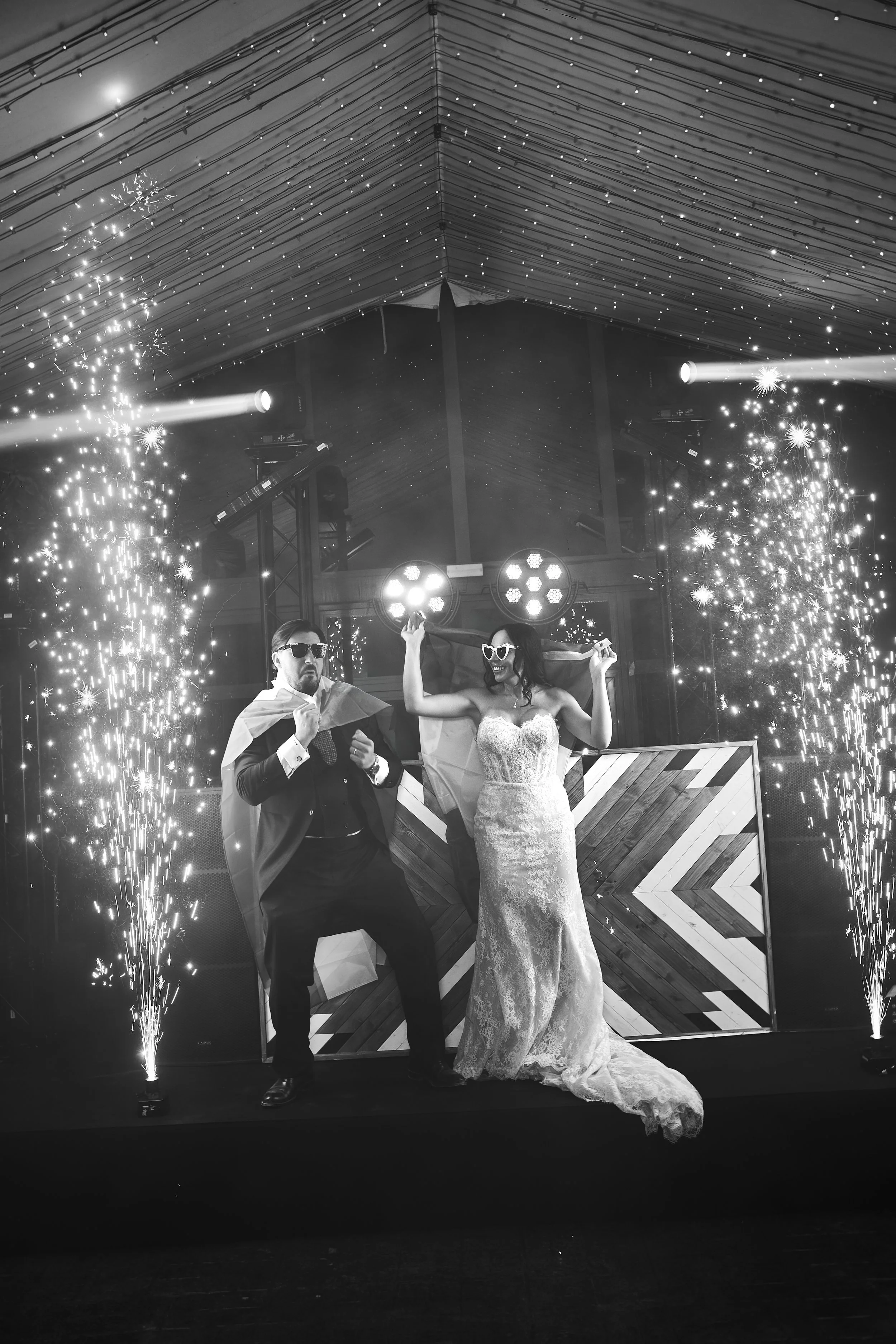 Pareja en boda celebrando con fuegos artificiales y efectos de iluminación en un escenario decorado con madera.