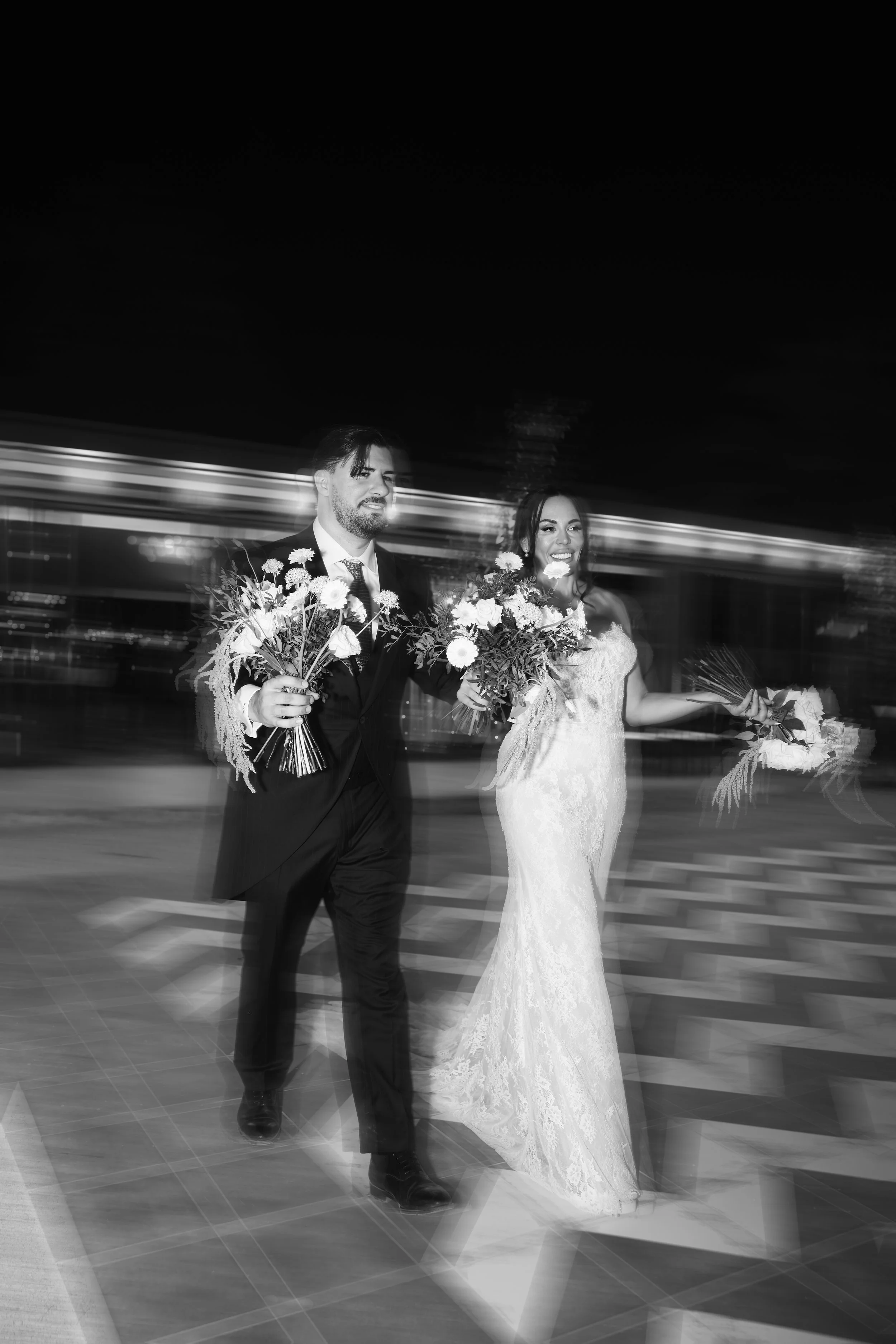 Pareja de novios bailando en su boda, ambos con ramos de flores, en un ambiente nocturno con movimiento de luces de fondo.