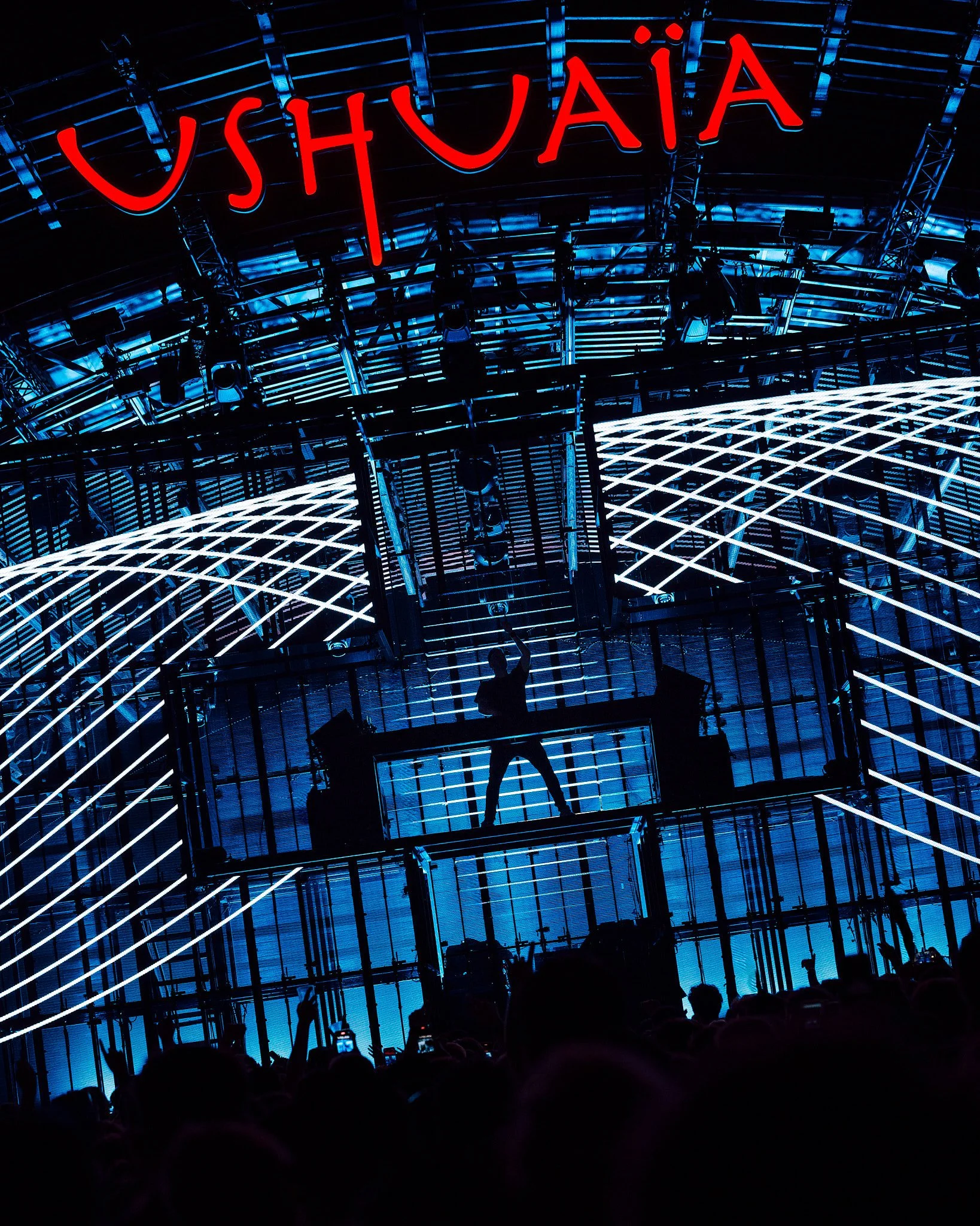 Martin Garrix, Un concierto de Ushuaïa con una estructura moderna iluminada en azul y líneas de luz blancas, con un DJ en el escenario y una multitud en primer plano.