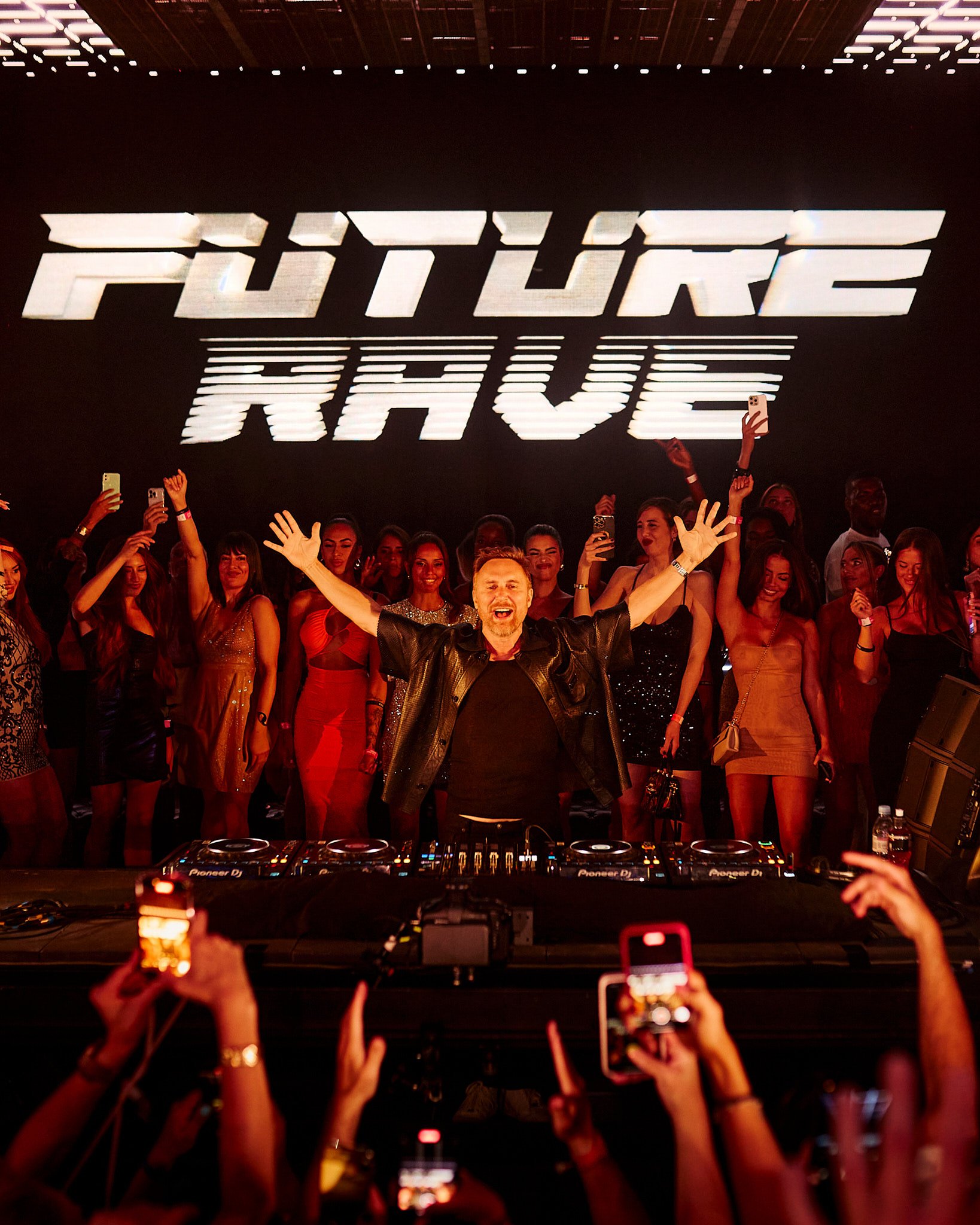 DJ en escenario con público en una fiesta, muestra la pantalla que dice 'FUTURE RAVE'.