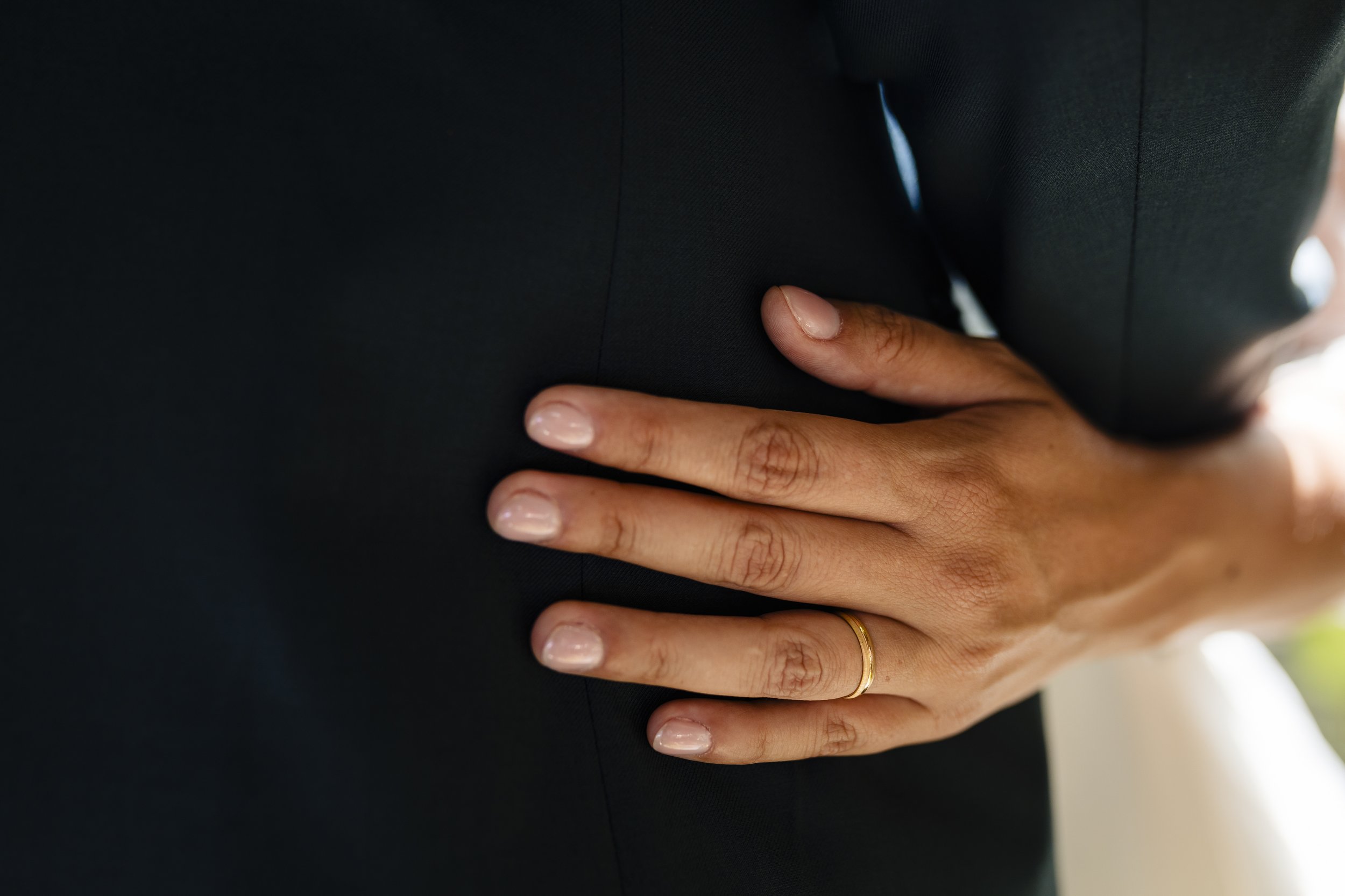 Mano con anillo en la cintura, tocando un traje negro.