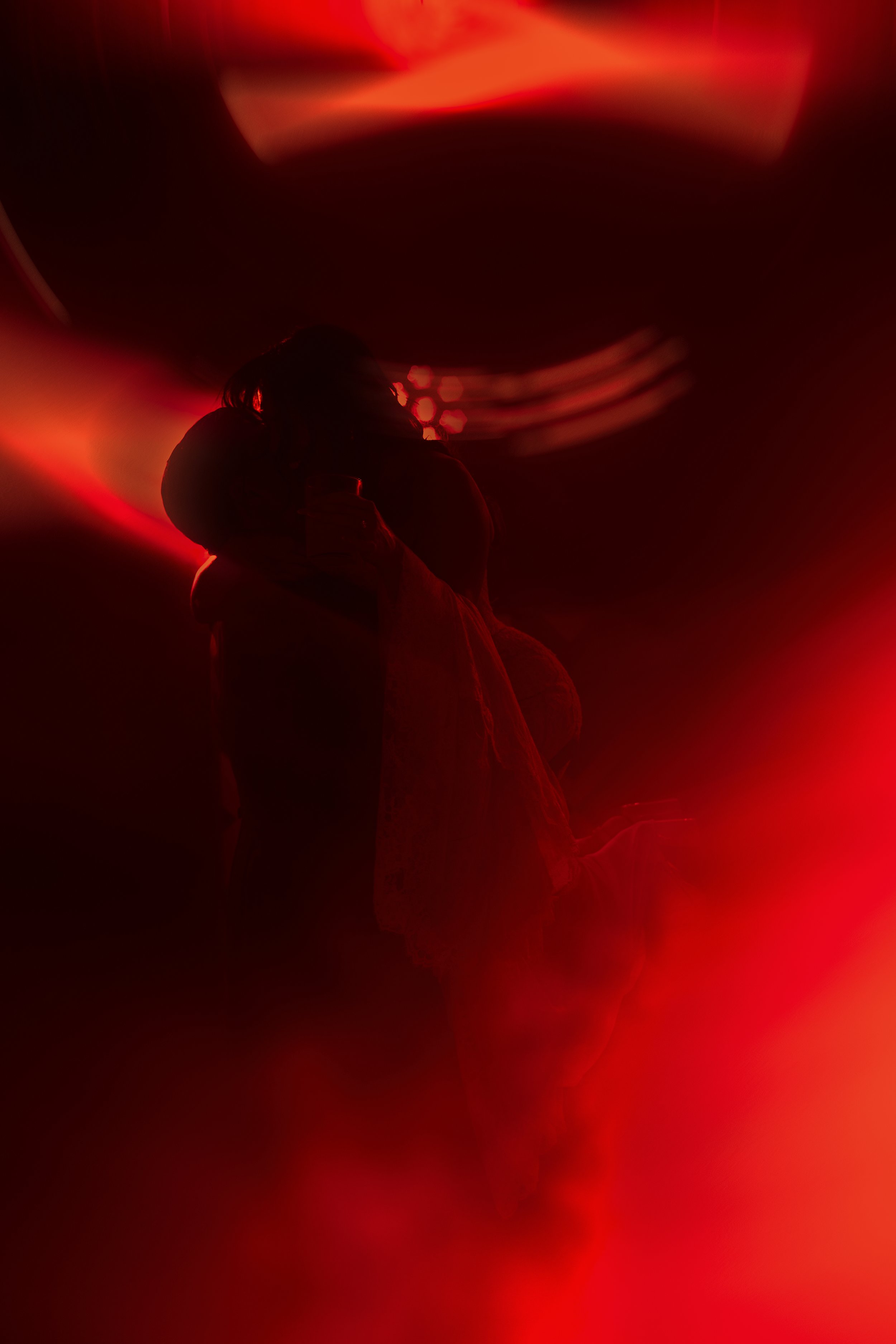 Silhouette de una pareja abrazándose en un entorno con luces rojas y efectos de luz difusos.