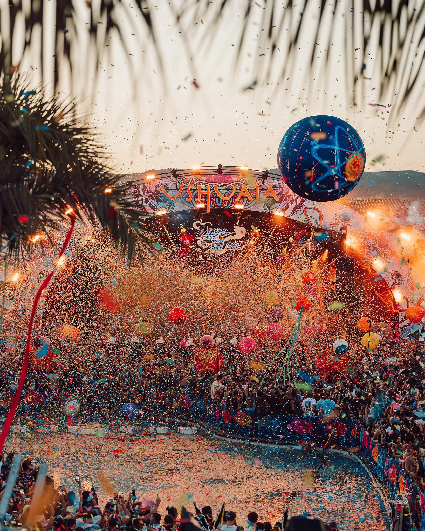 Concierto en Ushuaia con confeti y globos en el aire, escenario iluminado y multitud de personas disfrutando del evento.