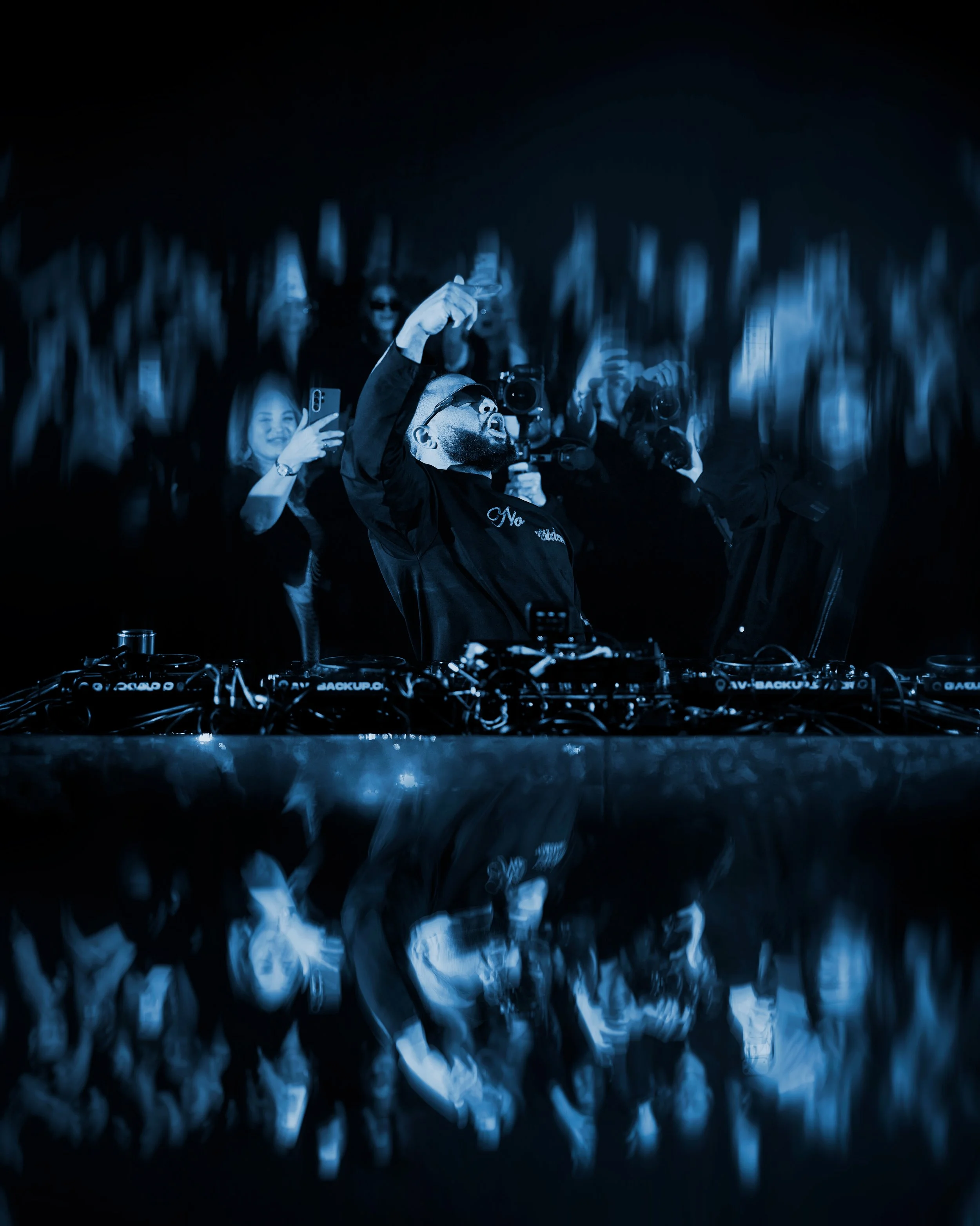 DJ en un espectáculo, rodeado de espectadores, con un efecto de reflejo y distorsión en la parte inferior.