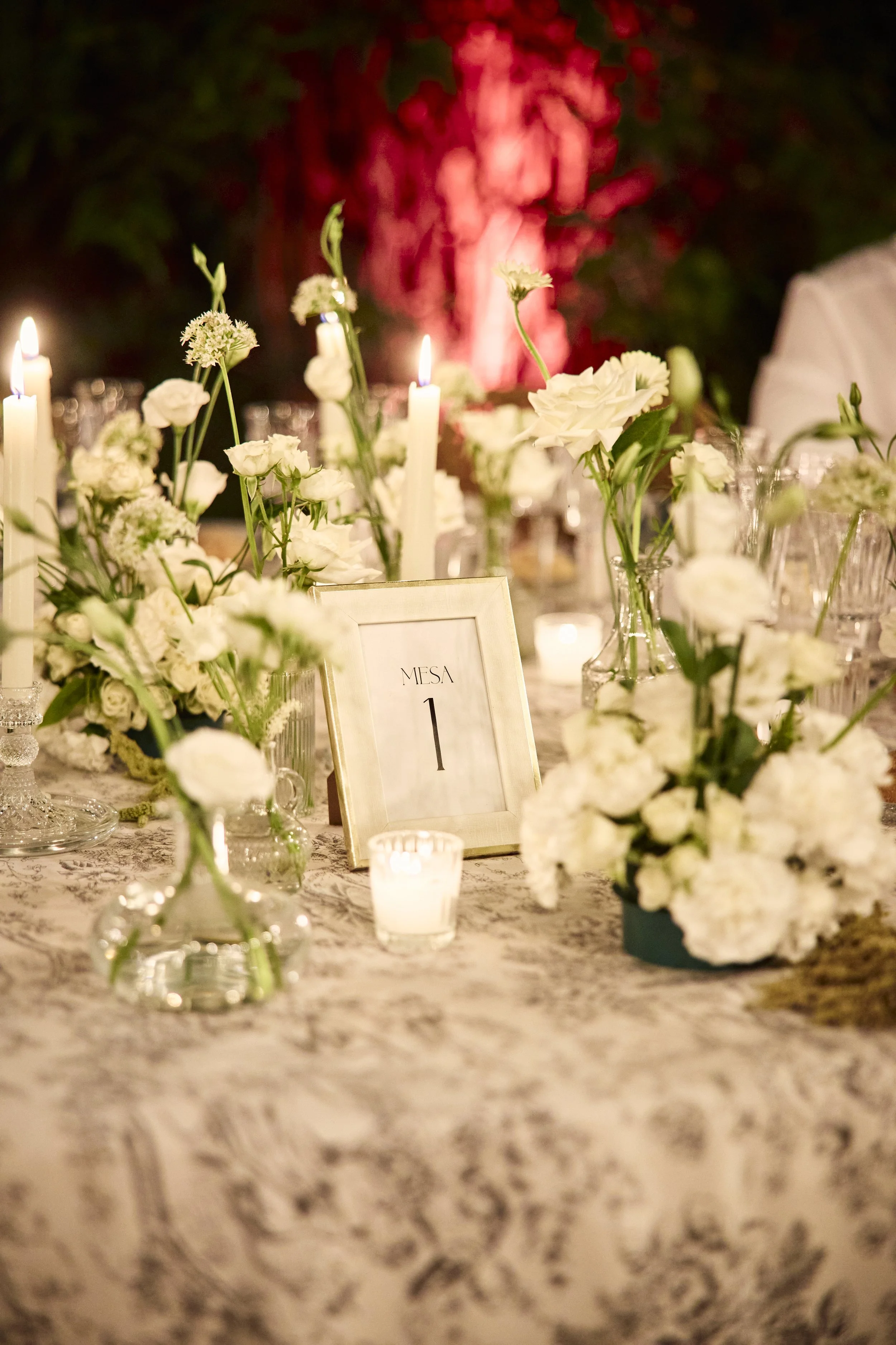 Mesa decorada con flores blancas, velas y una señal que dice 'mesa 1'.