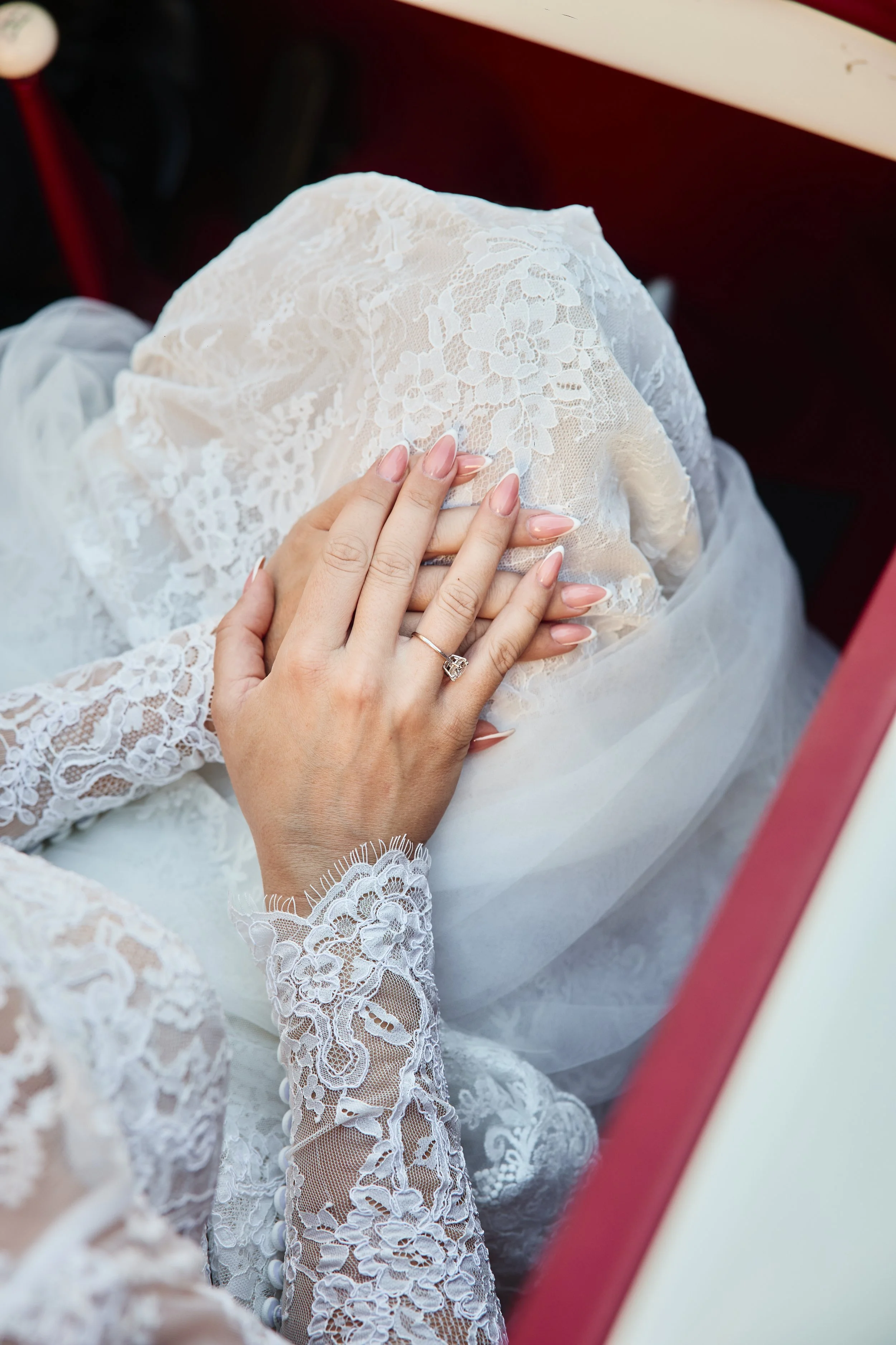 Mano con anillo de novia tocando vestido de encaje blanco con manga larga y detalles florales, vista desde arriba en un vestido nupcial.