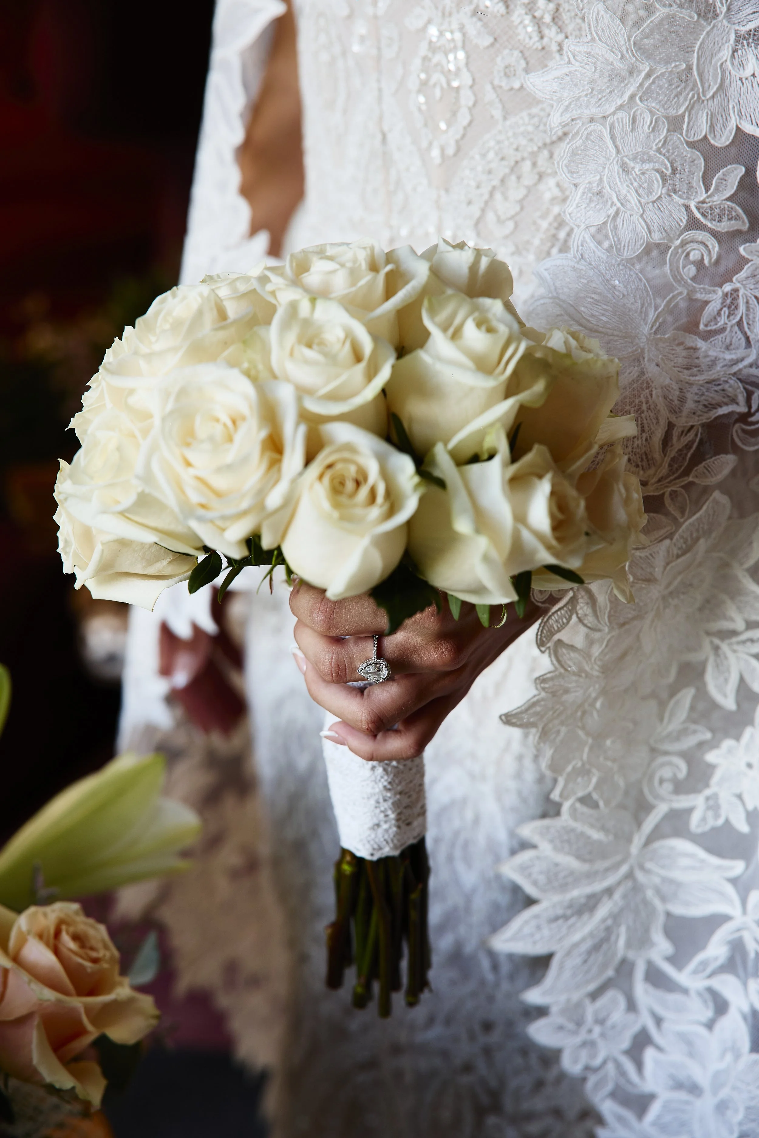 Mujer con vestido de novia sosteniendo ramos de rosas blancas.