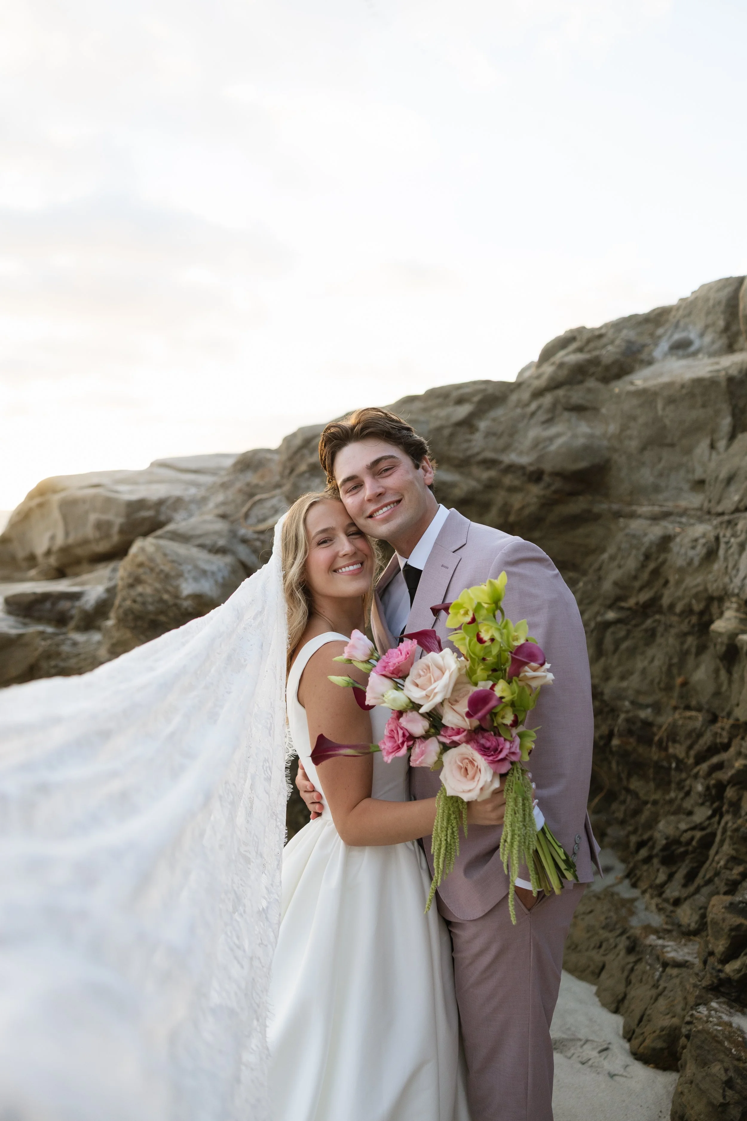 Newlywed couple on a San Diego beach at sunset holding a colorful modern bridal bouquet designed by San Diego wedding florist Isla Flor.