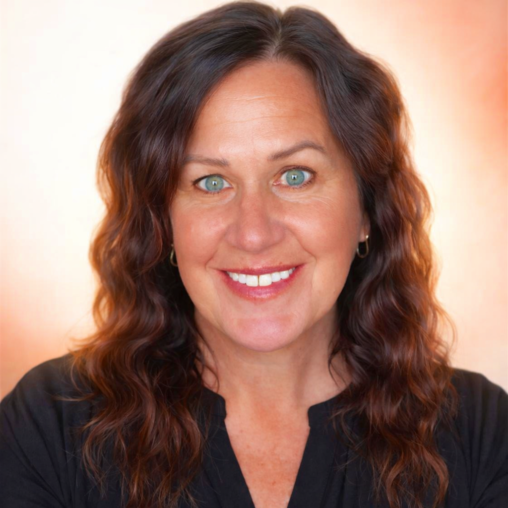 Close-up portrait of a woman with curly brown hair, blue eyes, fair skin, wearing small hoop earrings, smiling and wearing a black top.
