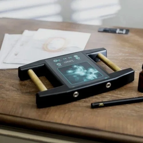 A portable electronic diagnostic device on a wooden table, with papers and a pen nearby.