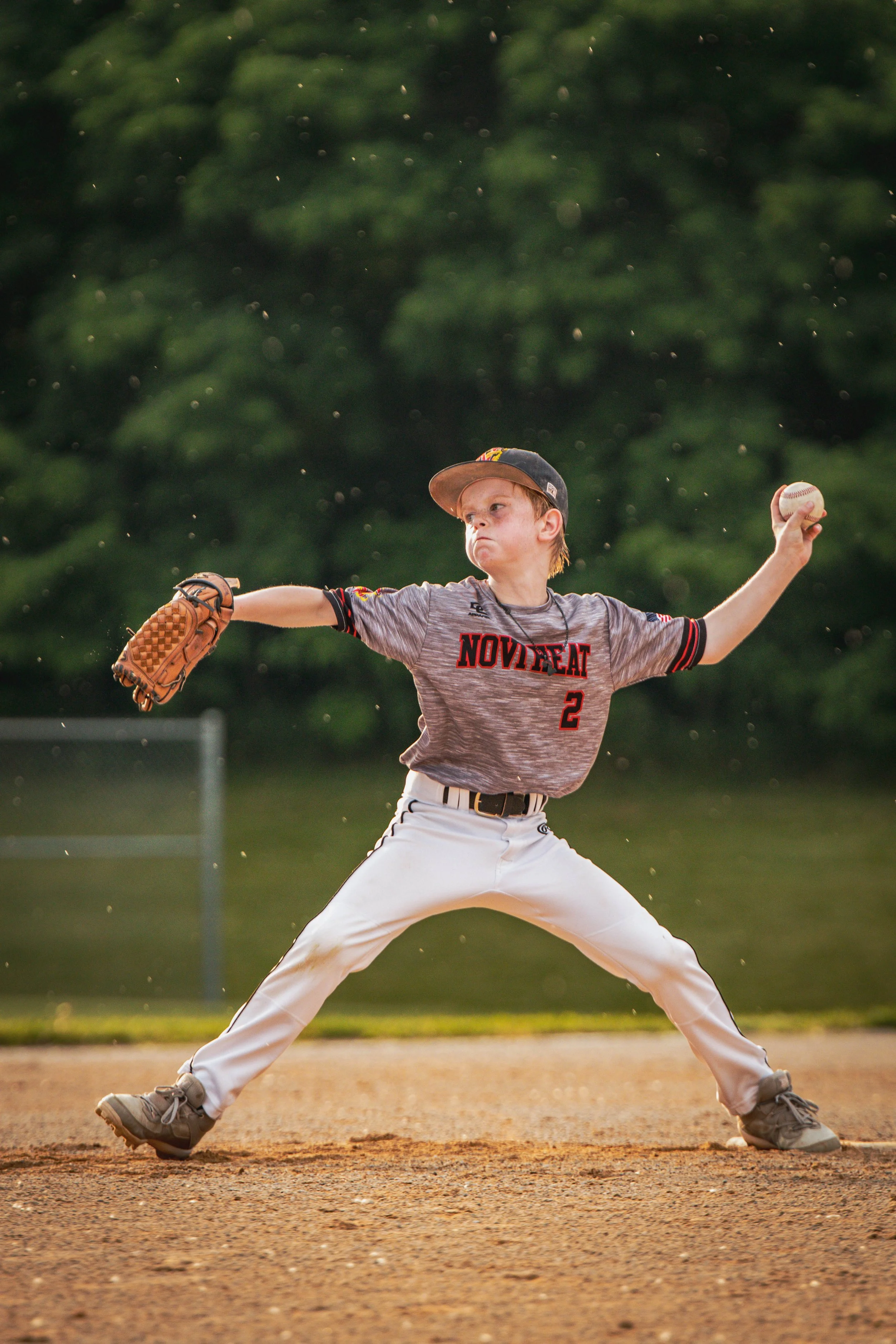 Young baseball player in a gray uniform with 'NOVAT' on the front, throwing a baseball with a focused expression.